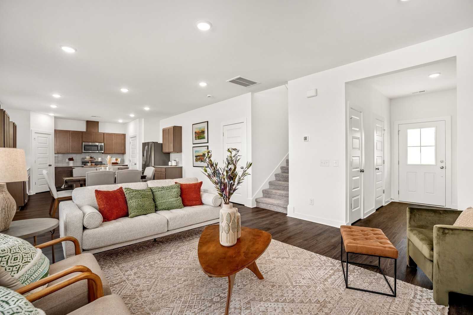 Modern open-concept living room with white sofa, wooden coffee table, rug, and adjacent kitchen in Davidson Homes The Gordon C, White House, TN