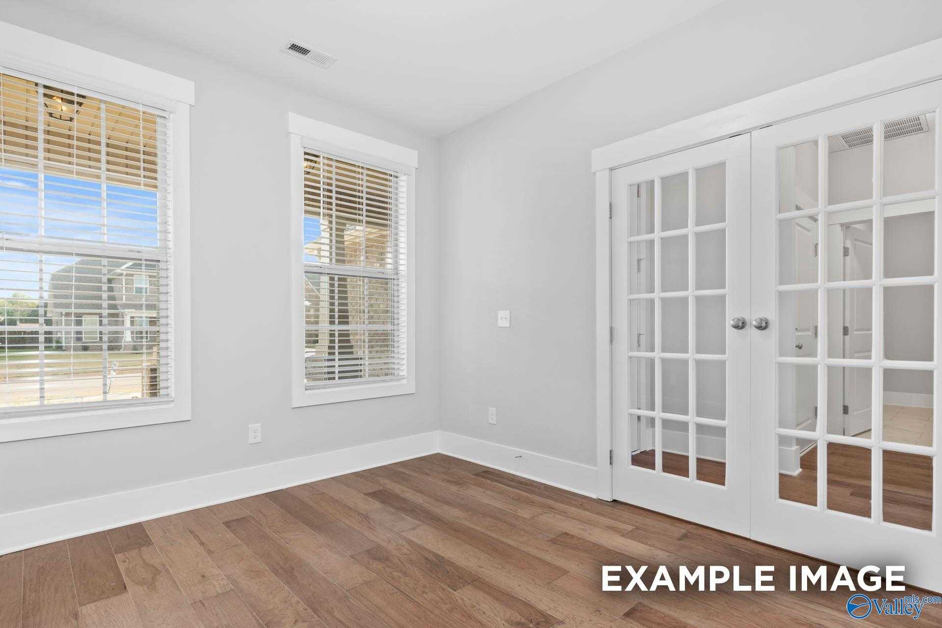 Bright living room with hardwood floors, white French doors, and large blinds-covered windows in Davidson Homes The Rockford, Meridianville, Alabama