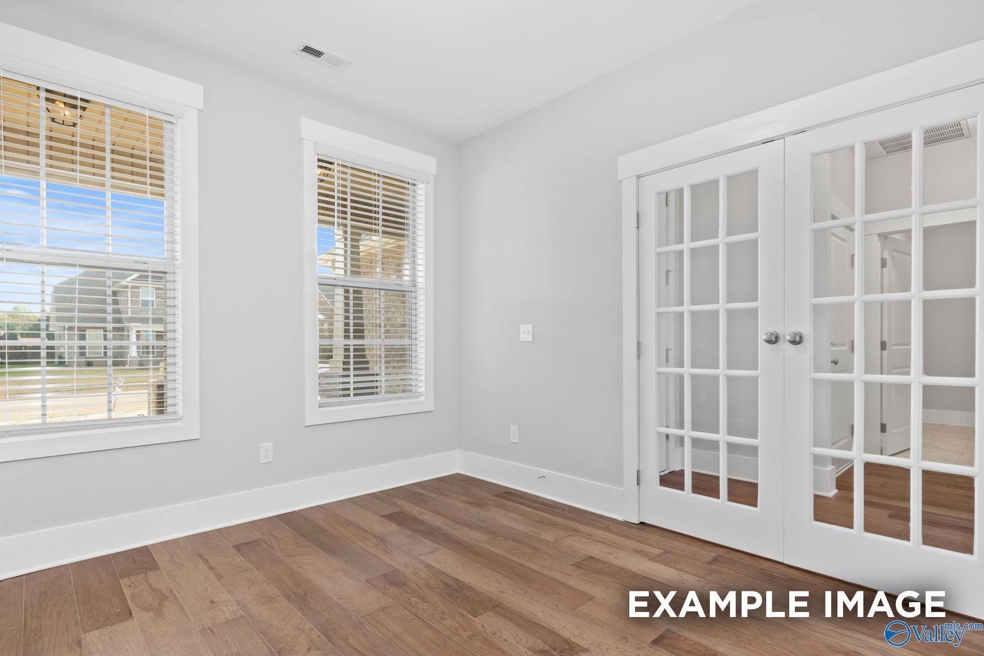 Bright airy room with light gray walls, hardwood floors, large blinds-covered windows, and white French doors in Davidson Homes The Rockford, Athens AL