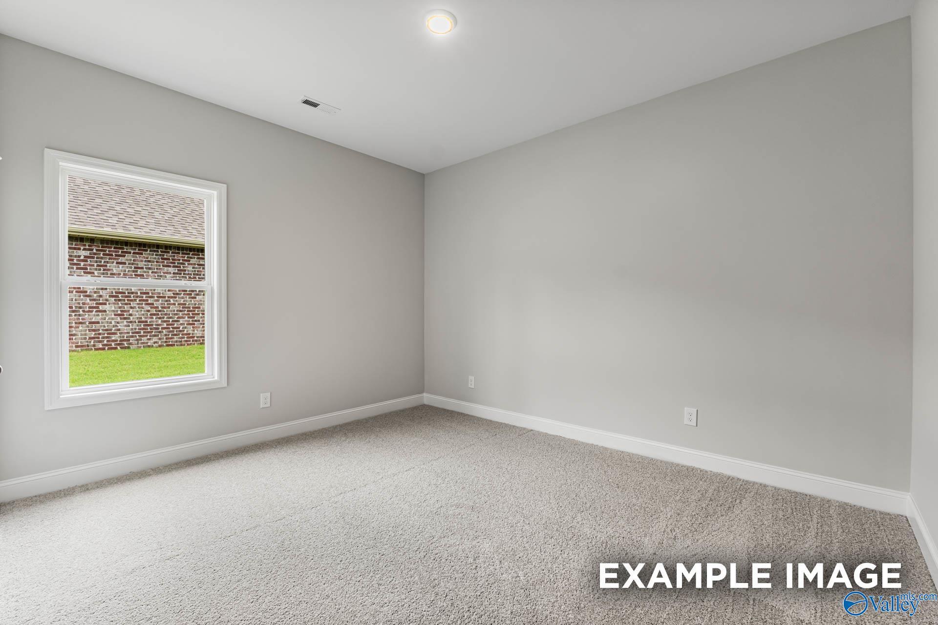 Bright secondary bedroom with gray walls, large window overlooking green yard, and neutral carpet in Davidson Homes The Daphne, Hazel Green, Alabama