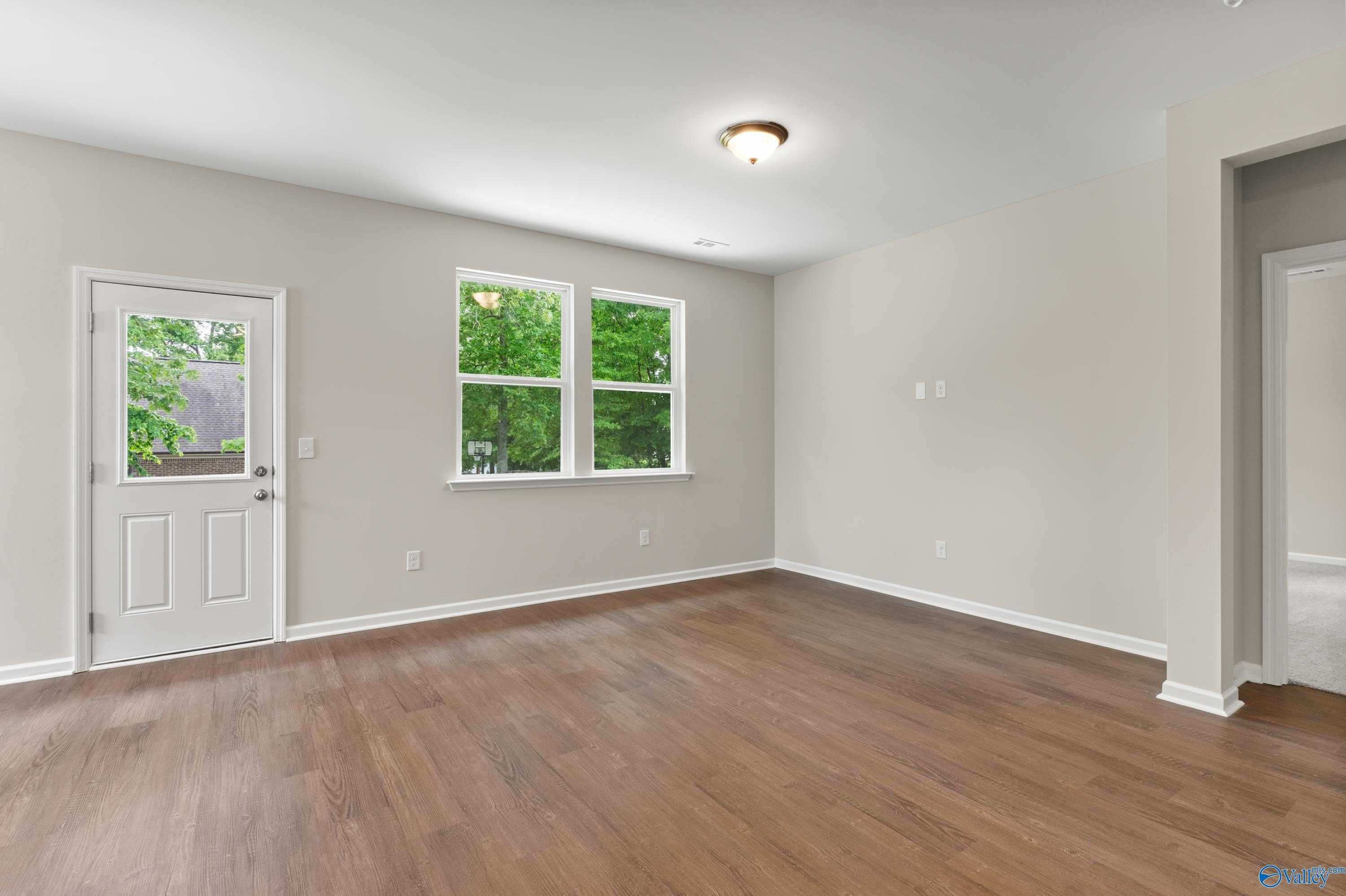 Empty living room with hardwood floors, large windows overlooking trees, in Davidson Homes The Phoenix, Bailey Park, Fayetteville Tennessee