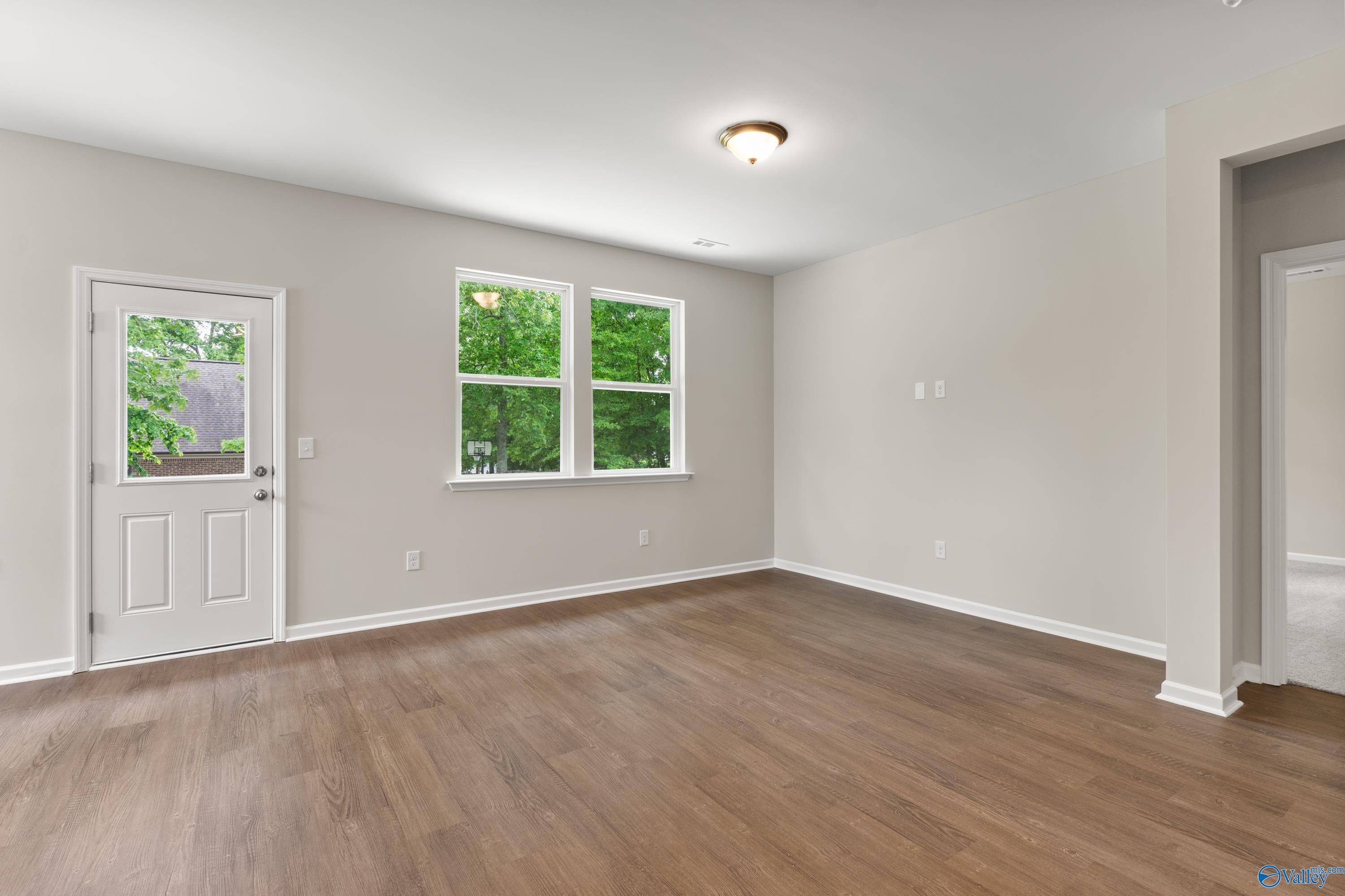 Bright empty living room with large windows, green views, hardwood floors, and beige walls in The Phoenix 3-bedroom home, Fayetteville TN