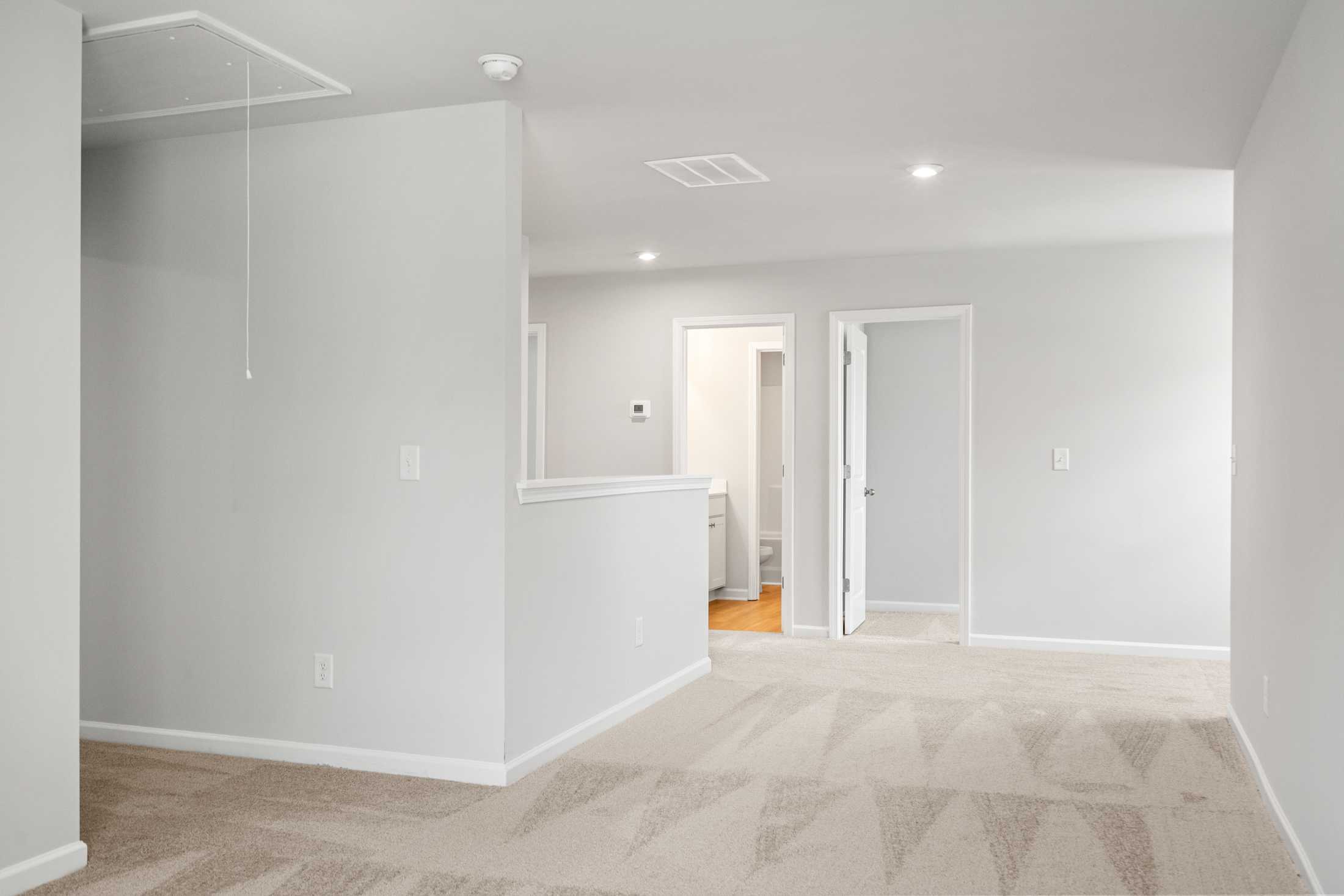 Spacious upstairs hallway in The Ash B at Wehunt Meadows, Hoschton GA, with gray walls, beige carpet, open railing, and bedroom doors