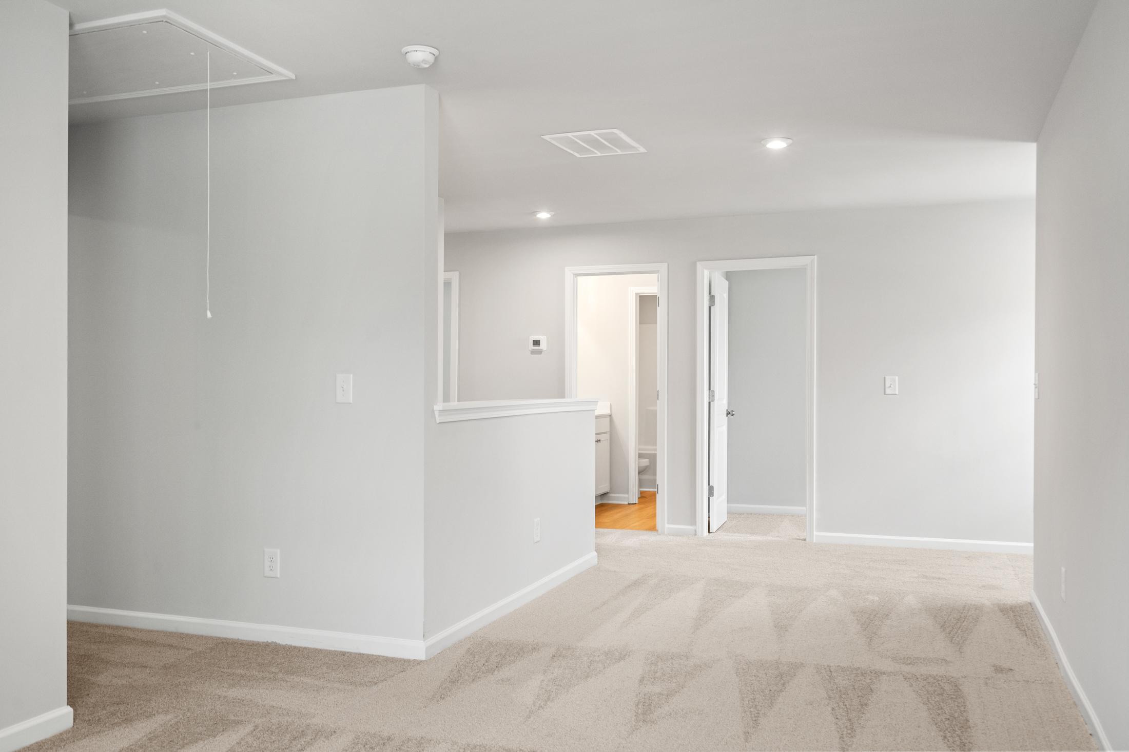 Spacious upstairs hallway in The Ash B at Wehunt Meadows, Hoschton GA, with gray walls, beige carpet, open railing, and bedroom doors