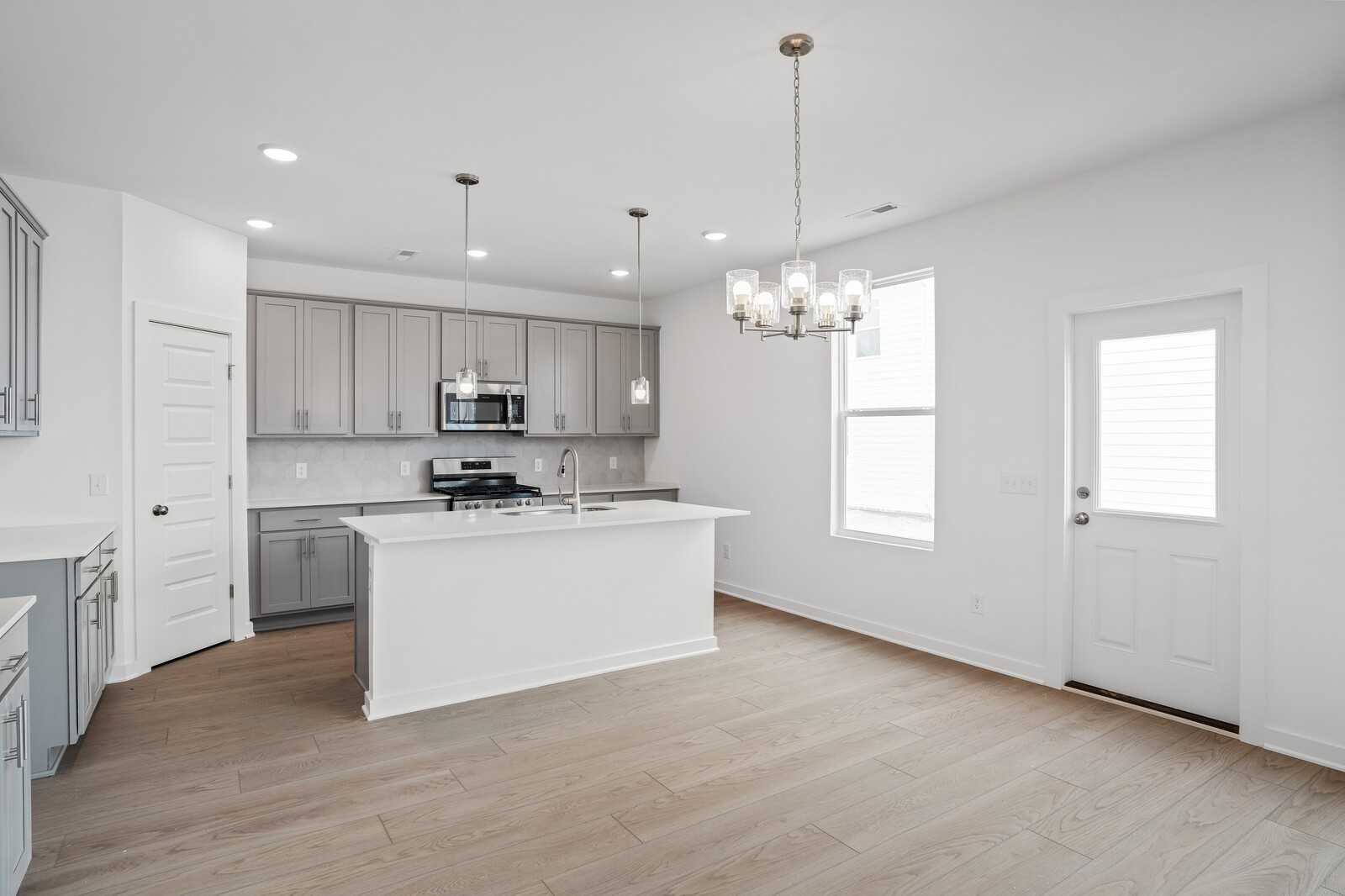 Modern white kitchen with large island, stainless appliances, pendant lights in The Logan B home, Calista Farms, White House, TN
