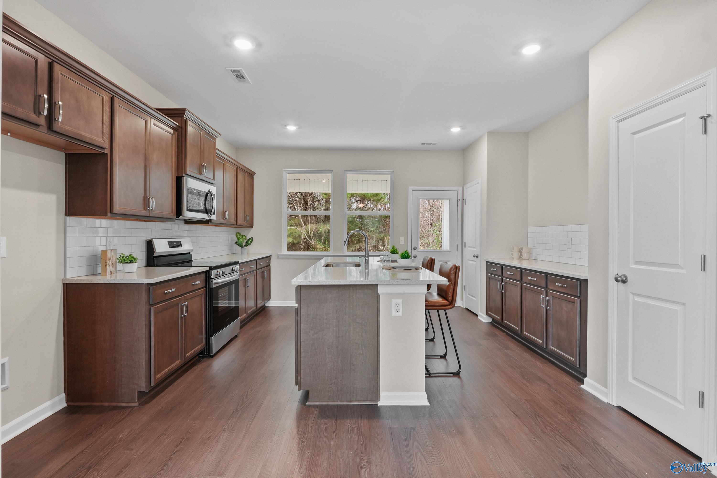 Modern kitchen featuring dark cabinets, stainless appliances, large island, subway tile backsplash, and hardwood floors in Davidson Homes The Stella, Hazel Green, AL