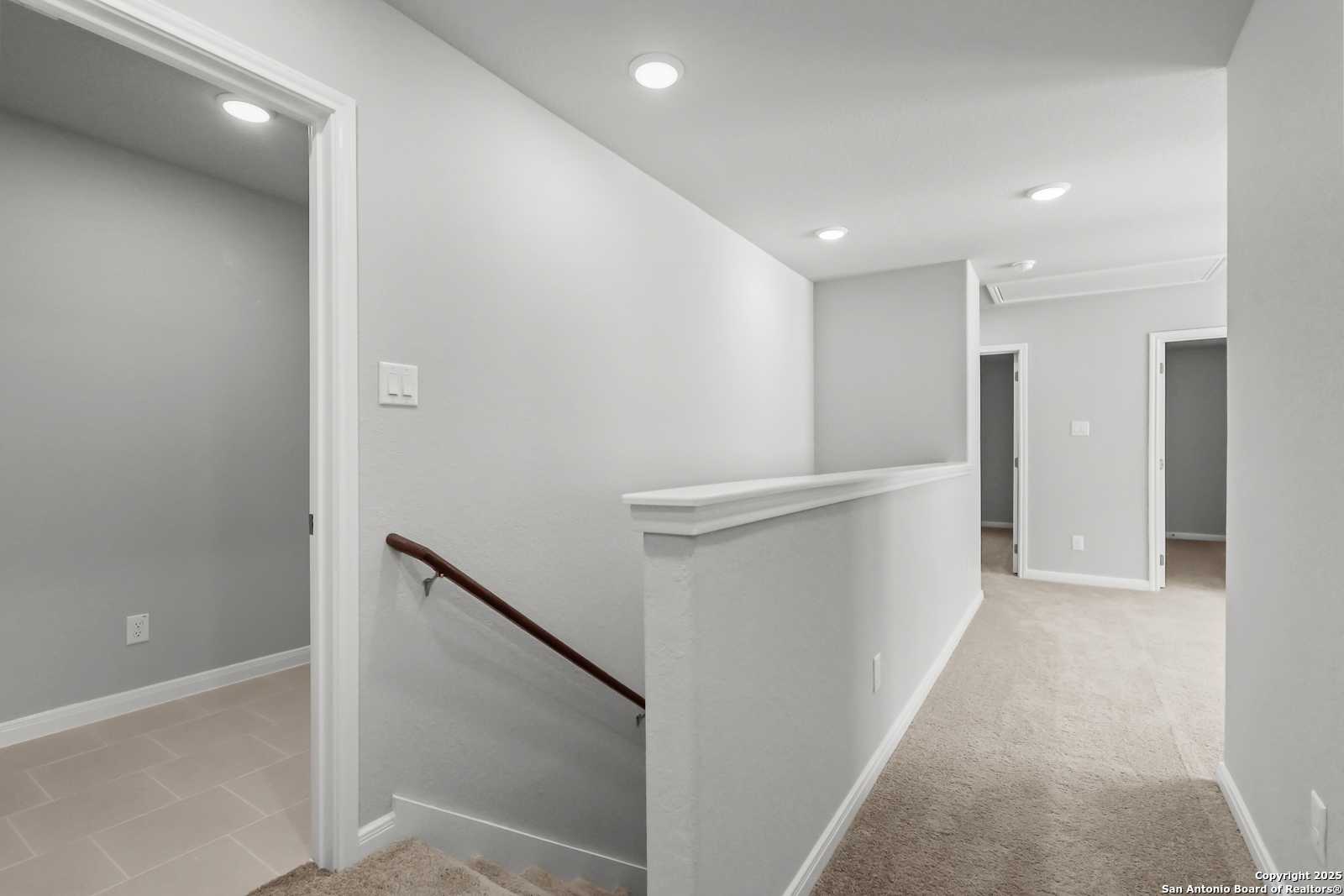 Bright second-floor hallway with gray walls, carpeted floors, and staircase in The Gillian C 5-bedroom home, San Antonio