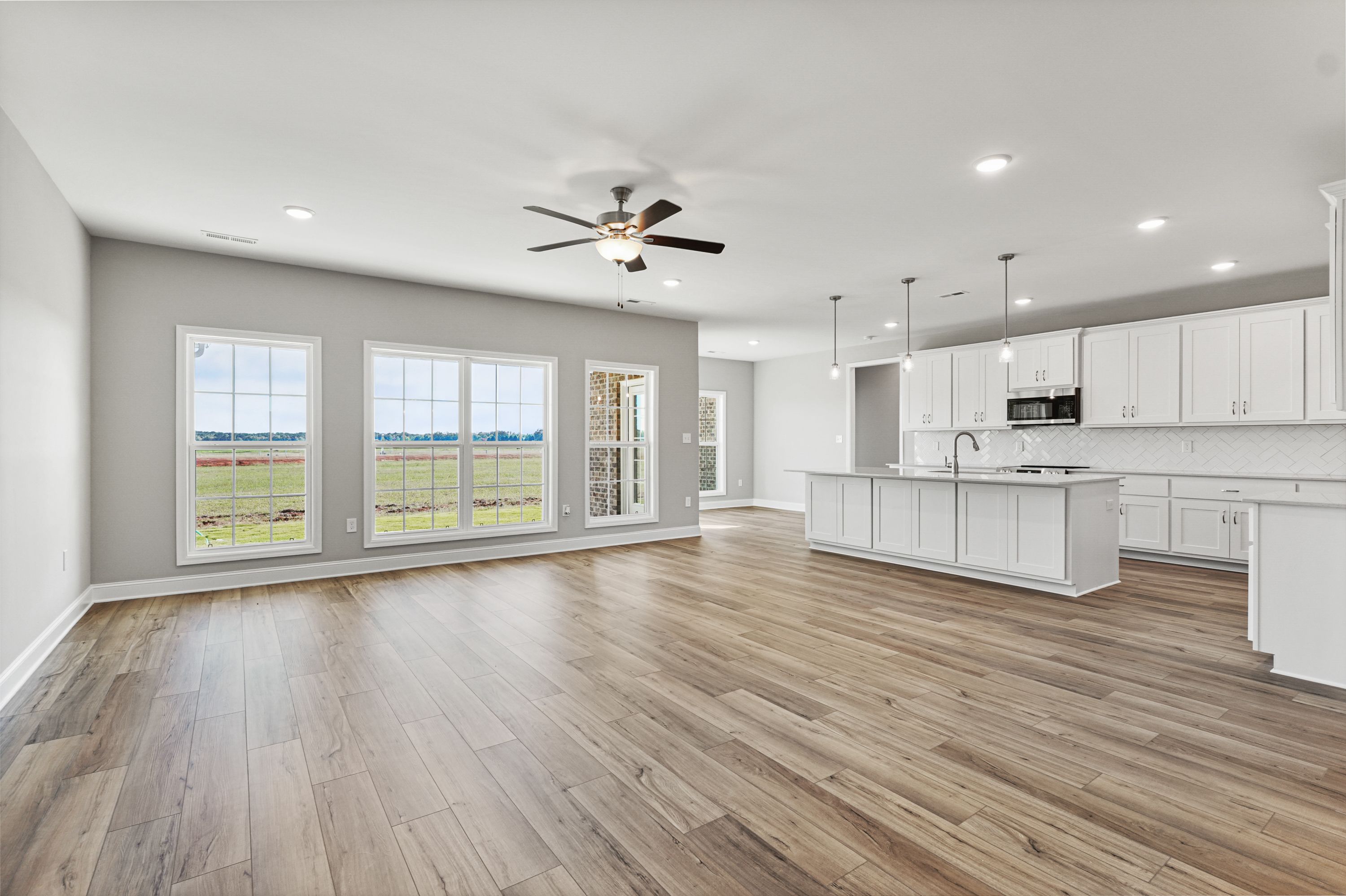 Spacious open-concept kitchen-living area in The Valencia home with large field-view windows, white island cabinets, hardwood floors