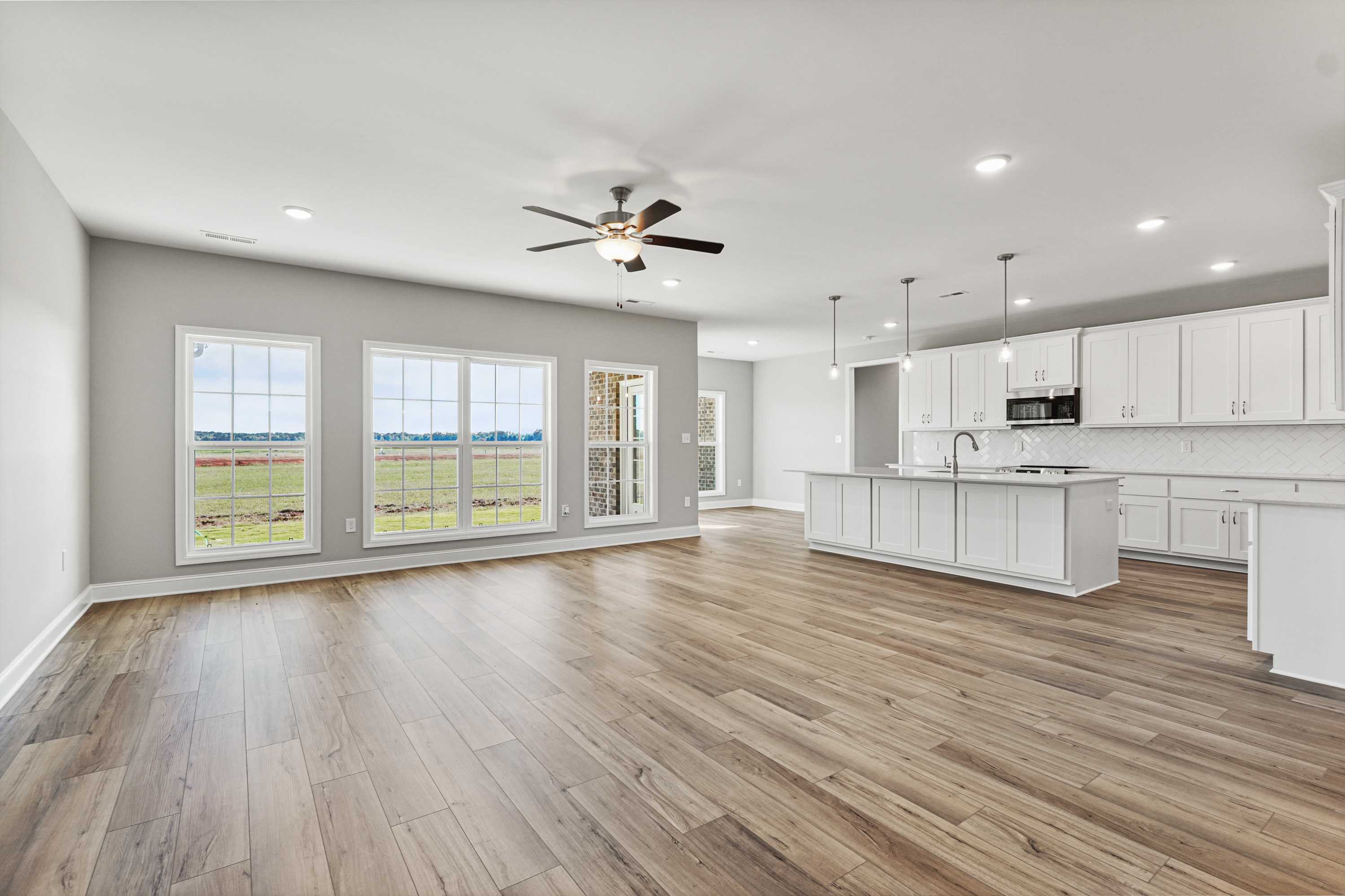 Spacious open-concept kitchen-living area in The Valencia home with large field-view windows, white island cabinets, hardwood floors