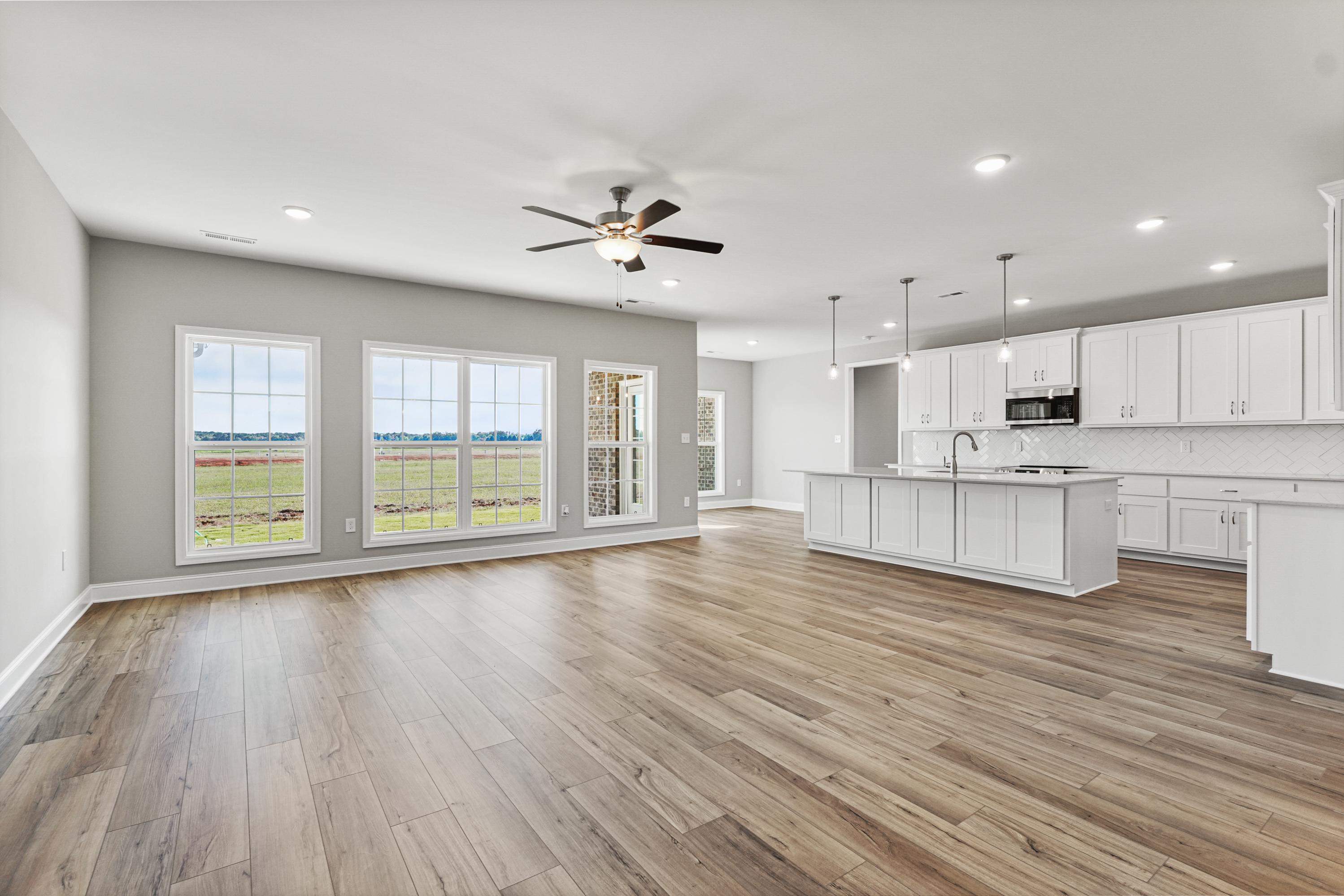 Spacious open-concept kitchen-living area in The Valencia home with large field-view windows, white island cabinets, hardwood floors