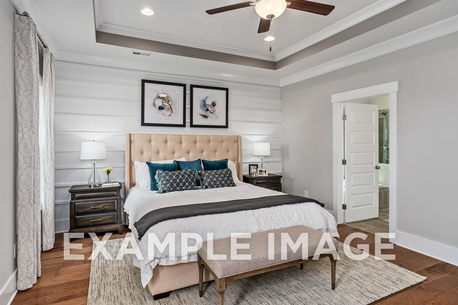 Spacious master bedroom in The Harrison B featuring beige upholstered bed, teal pillows, shiplap walls, ceiling fan, and en-suite bath
