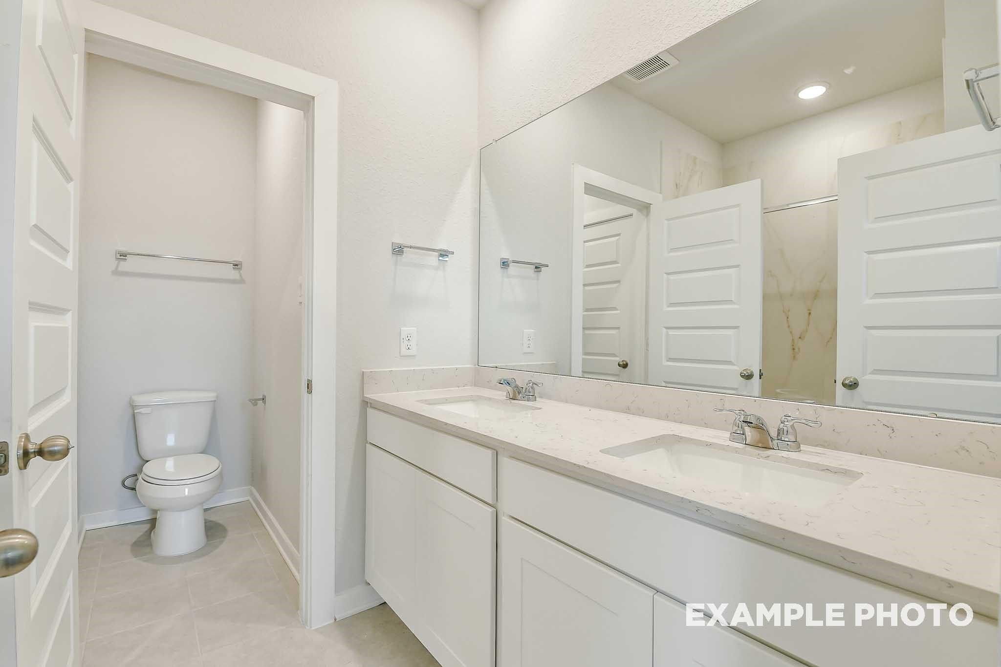 Modern double-sink vanity with quartz counters, large mirror, and walk-in shower in Davidson Homes The Colorado G, Conroe, Texas