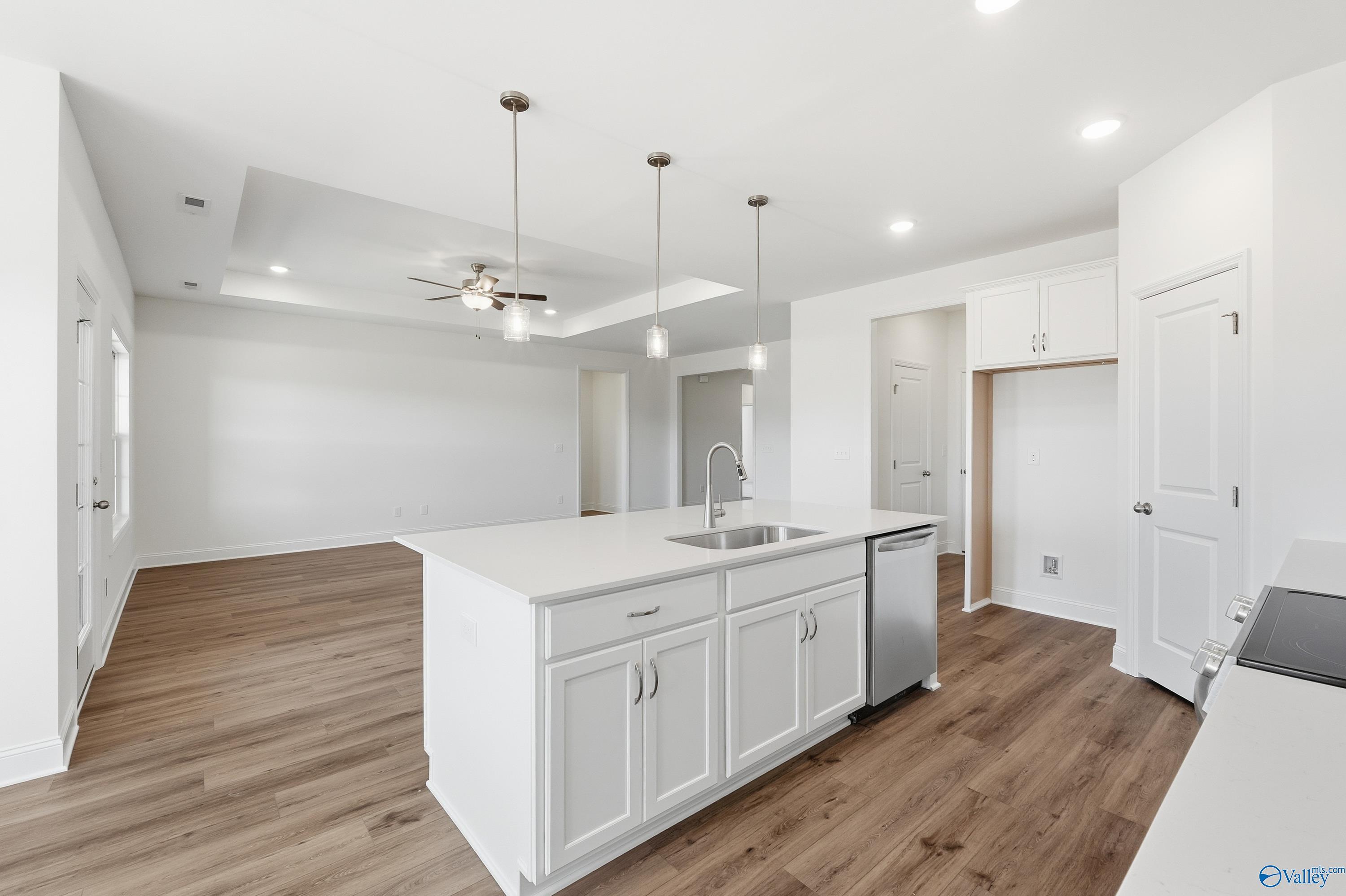 Modern white kitchen island with sink and dishwasher on hardwood floors, open layout in The Montgomery by Davidson Homes, Meridianville AL