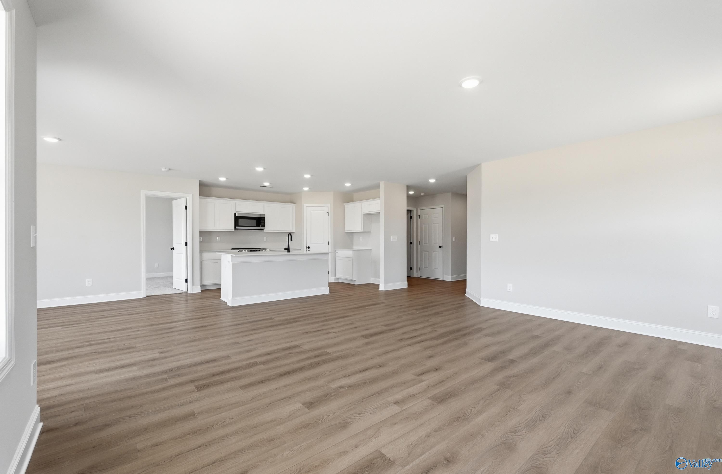 Open-concept kitchen with white cabinets, island sink and wood flooring in The Franklin V 3-bedroom home, Athens, Alabama
