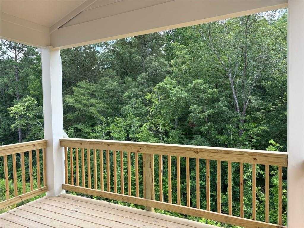 Covered rear deck with wooden railing and white columns overlooking lush green forest in Davidson Homes The Hickory B, Riverwood, Dallas, Georgia