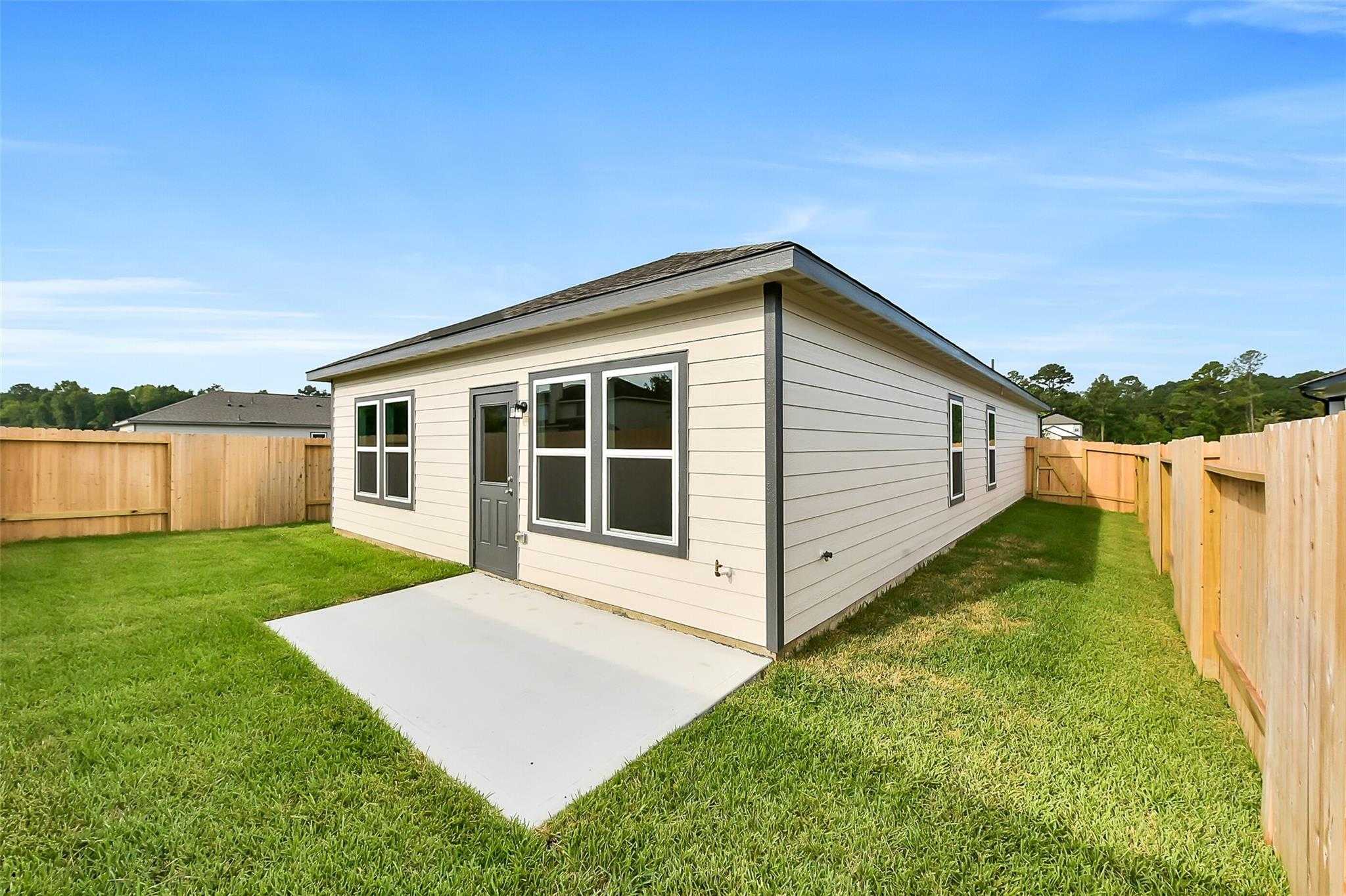 Beige single-story Davidson Homes The Frio G exterior with concrete patio, lush green lawn, wooden privacy fence in The Villages at WestPointe, Dayton, Texas