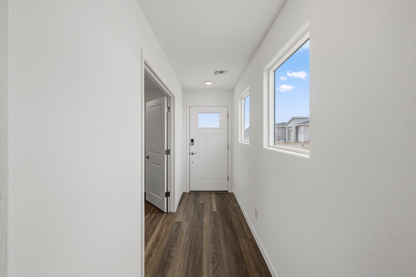 Bright entry hallway in The Raleigh by Davidson Homes with white walls, wood-look flooring, front door, and windows.