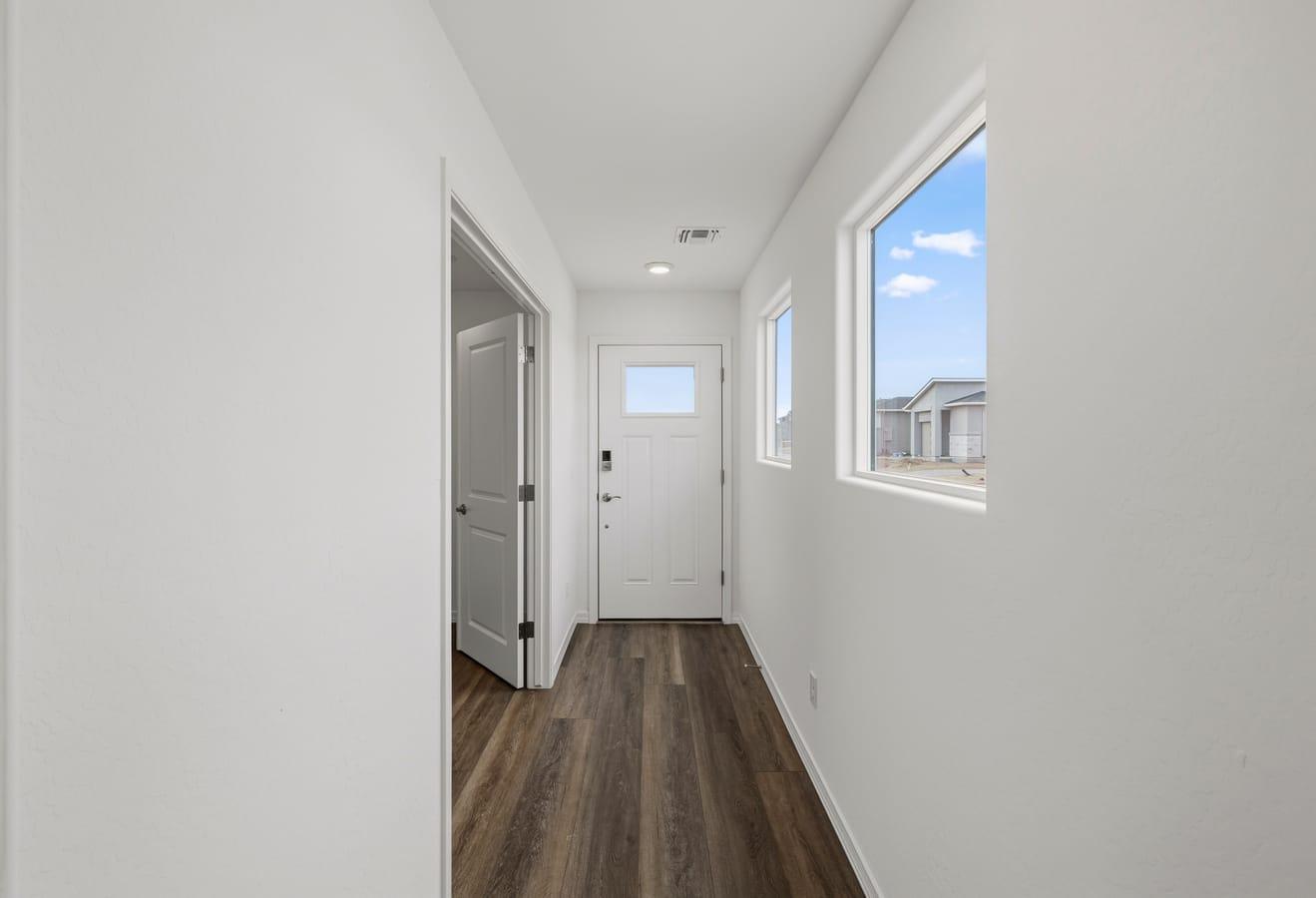 Bright entry hallway in The Raleigh by Davidson Homes with white walls, wood-look flooring, front door, and windows.