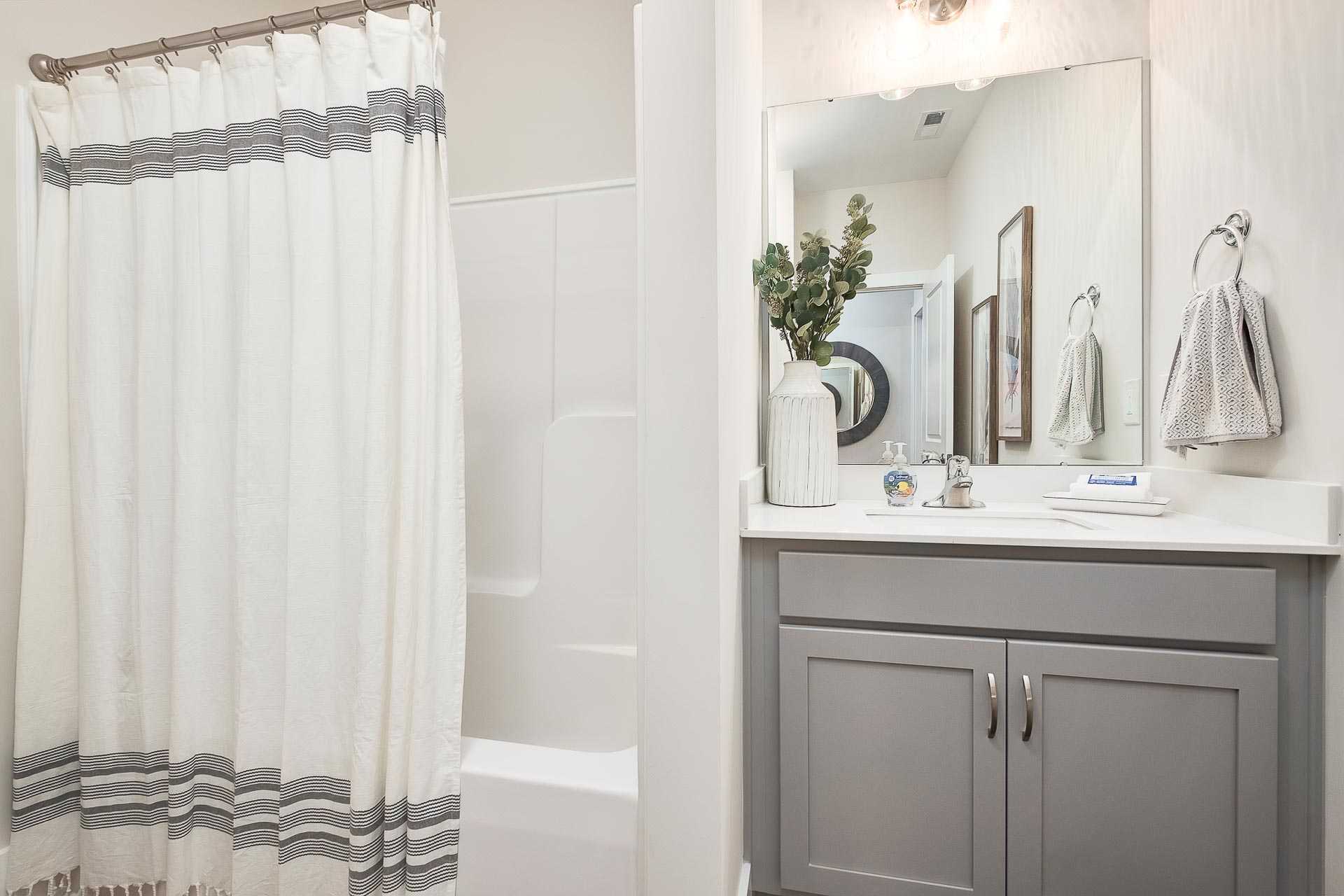 Spacious master bathroom in The Everett C featuring white subway tile tub shower, gray vanity, and modern mirror lighting