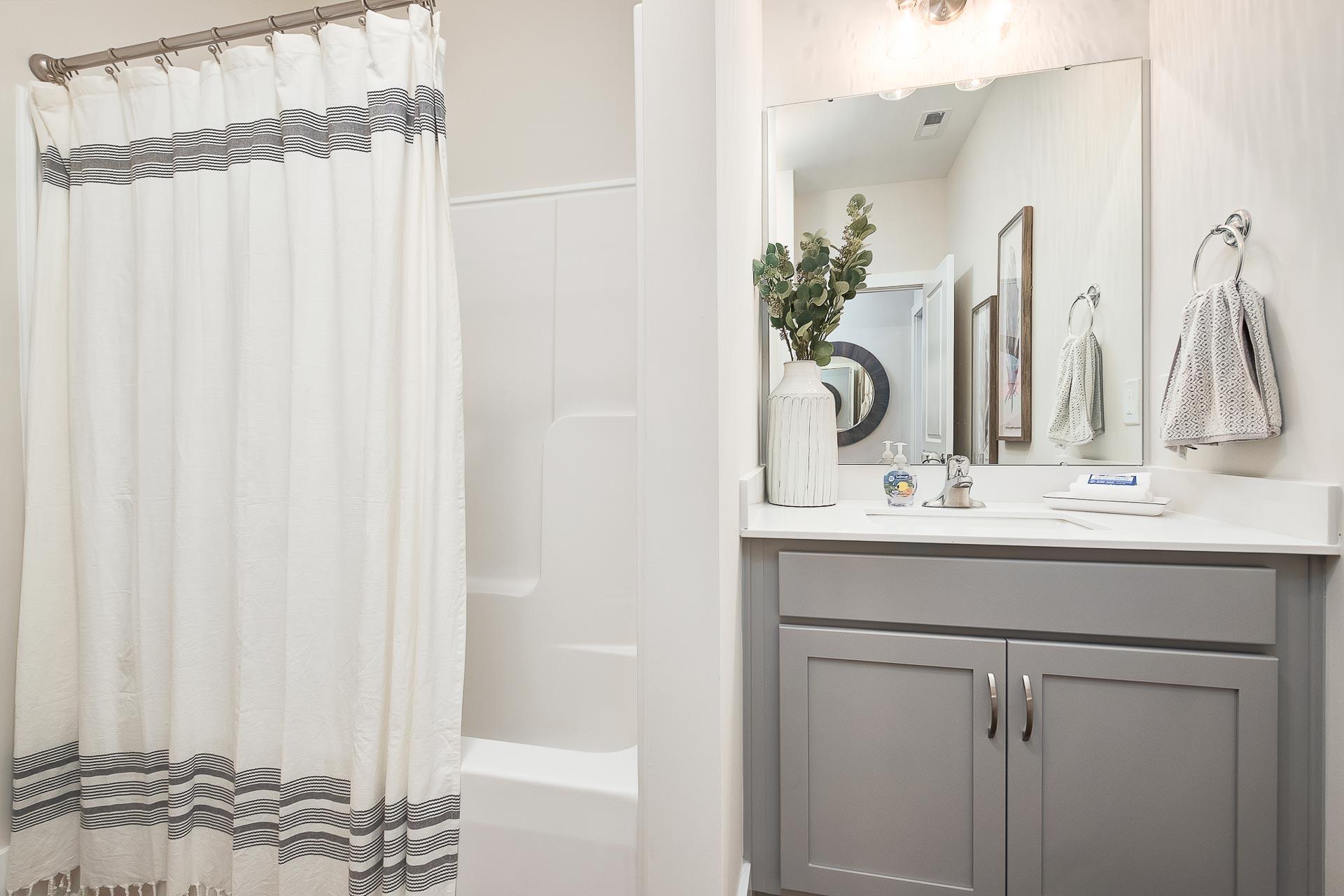 Modern master bathroom in The Everett featuring bathtub shower combo, gray vanity, and striped curtains