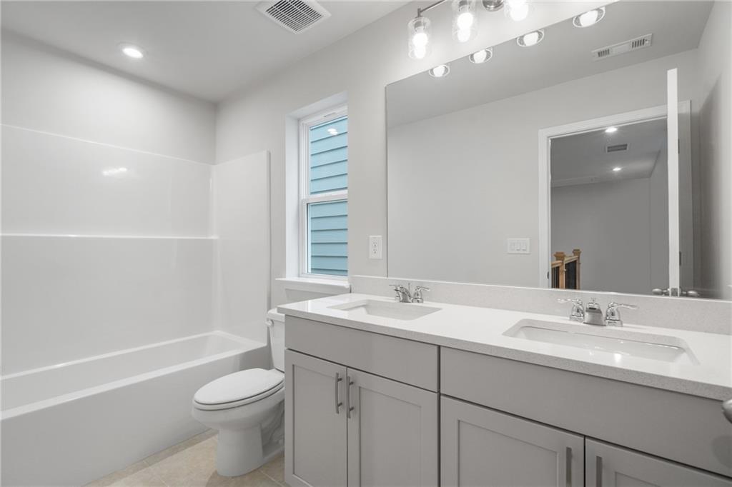 Bright secondary bathroom with double vanity sinks, soaking tub, and large mirror in Davidson Homes The Cary A, Kennesaw, GA