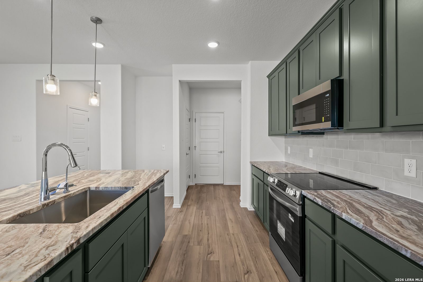 Modern kitchen with green cabinets, granite countertops, and stainless appliances in The Brazos B home in Agave, San Antonio.