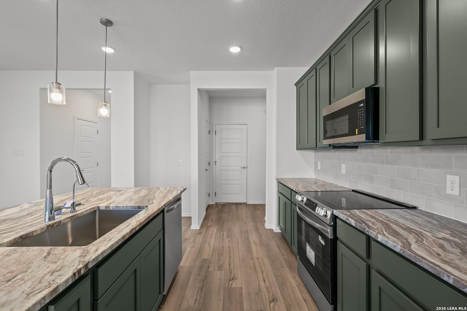 Modern kitchen with green cabinets, granite countertops, and stainless appliances in The Brazos B home in Agave, San Antonio.