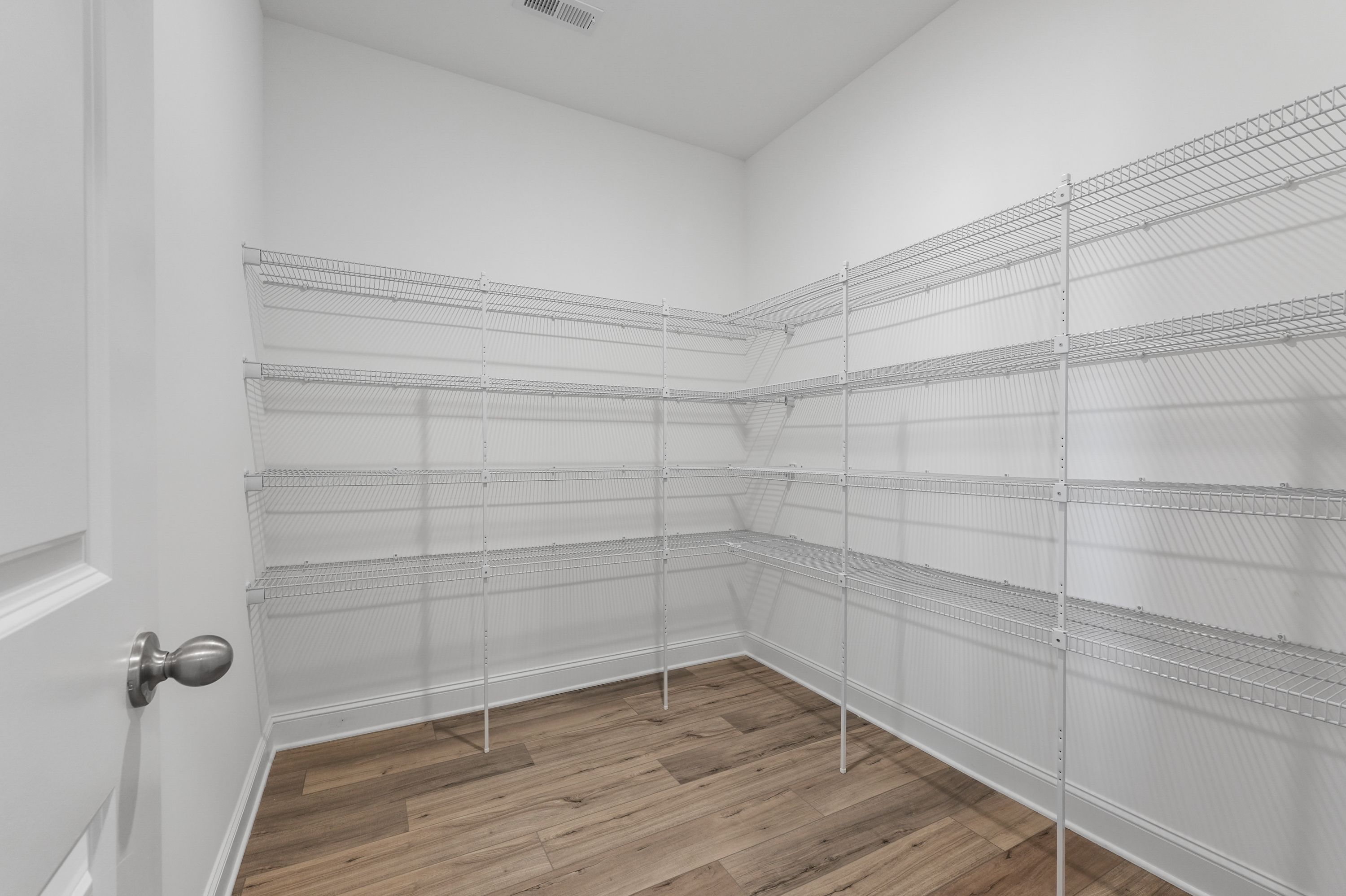 Spacious walk-in closet in The Valencia home featuring white wire shelving, hardwood floors, Davidson Homes design