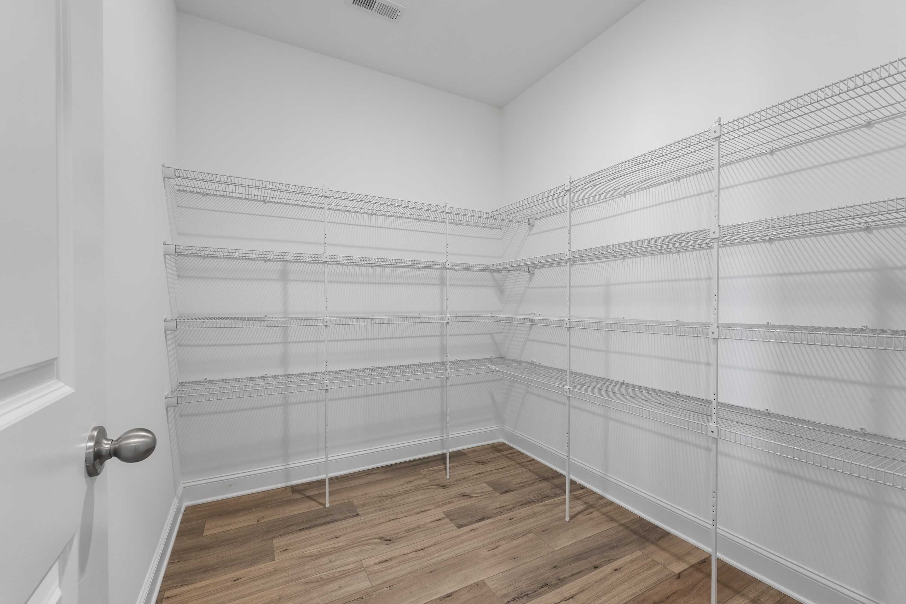 Spacious walk-in closet in The Valencia home featuring white wire shelving, hardwood floors, Davidson Homes design