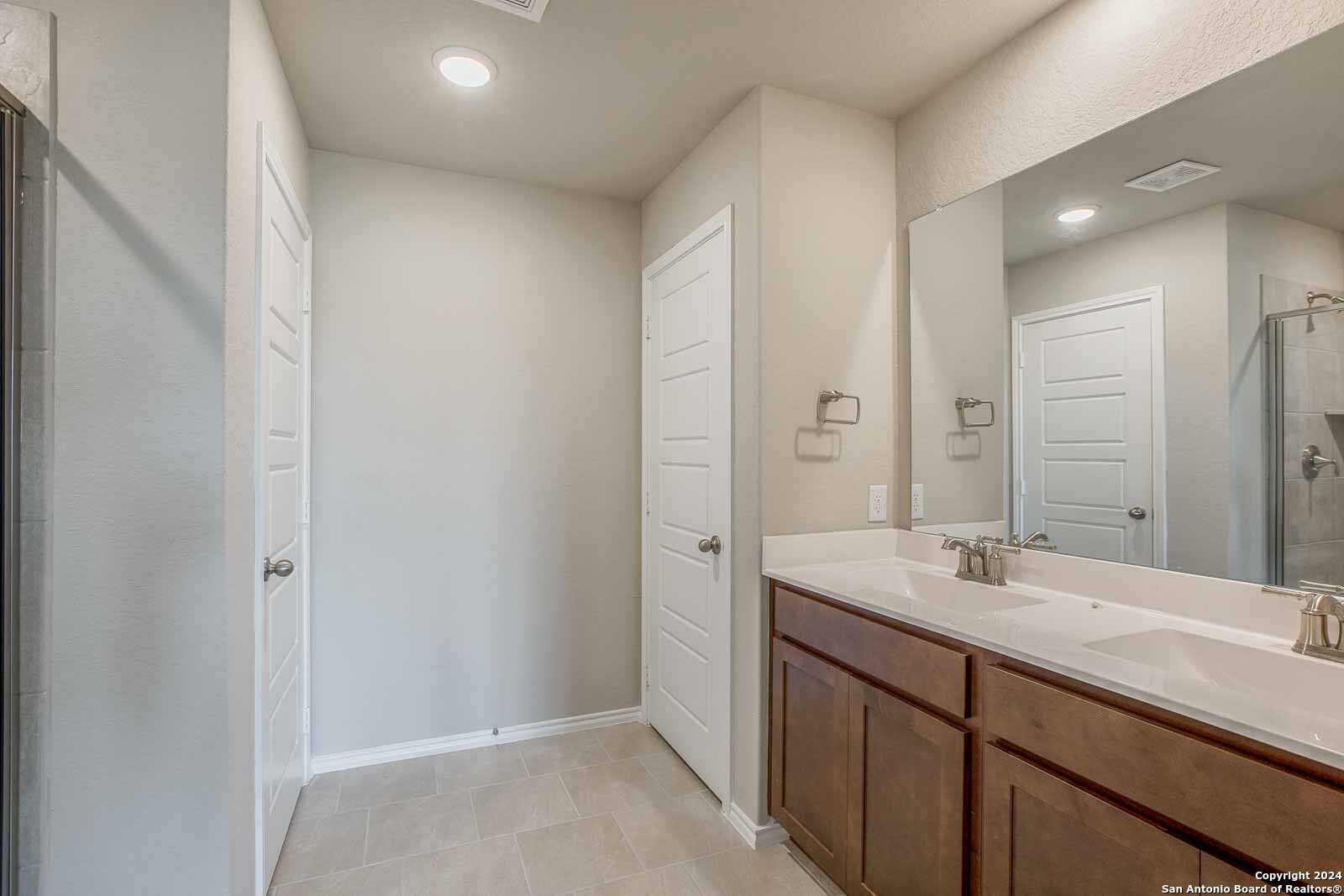 Modern master bathroom featuring double vanity, large mirror, and glass shower enclosure in Davidson Homes The Murray H, Seguin, Texas