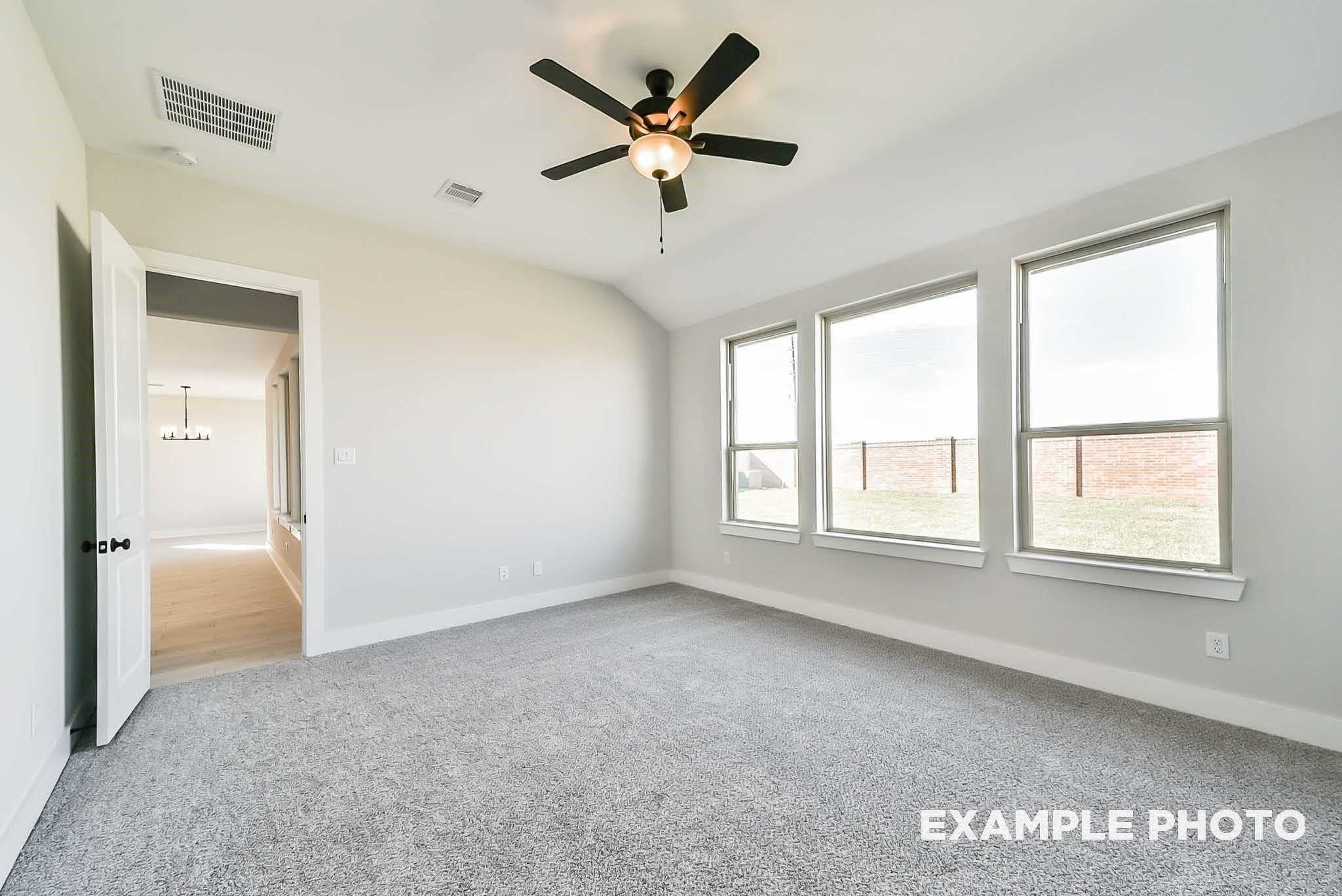 Spacious bedroom with ceiling fan, three large windows, and gray carpet in Davidson Homes The Philip C, Rosharon, Texas