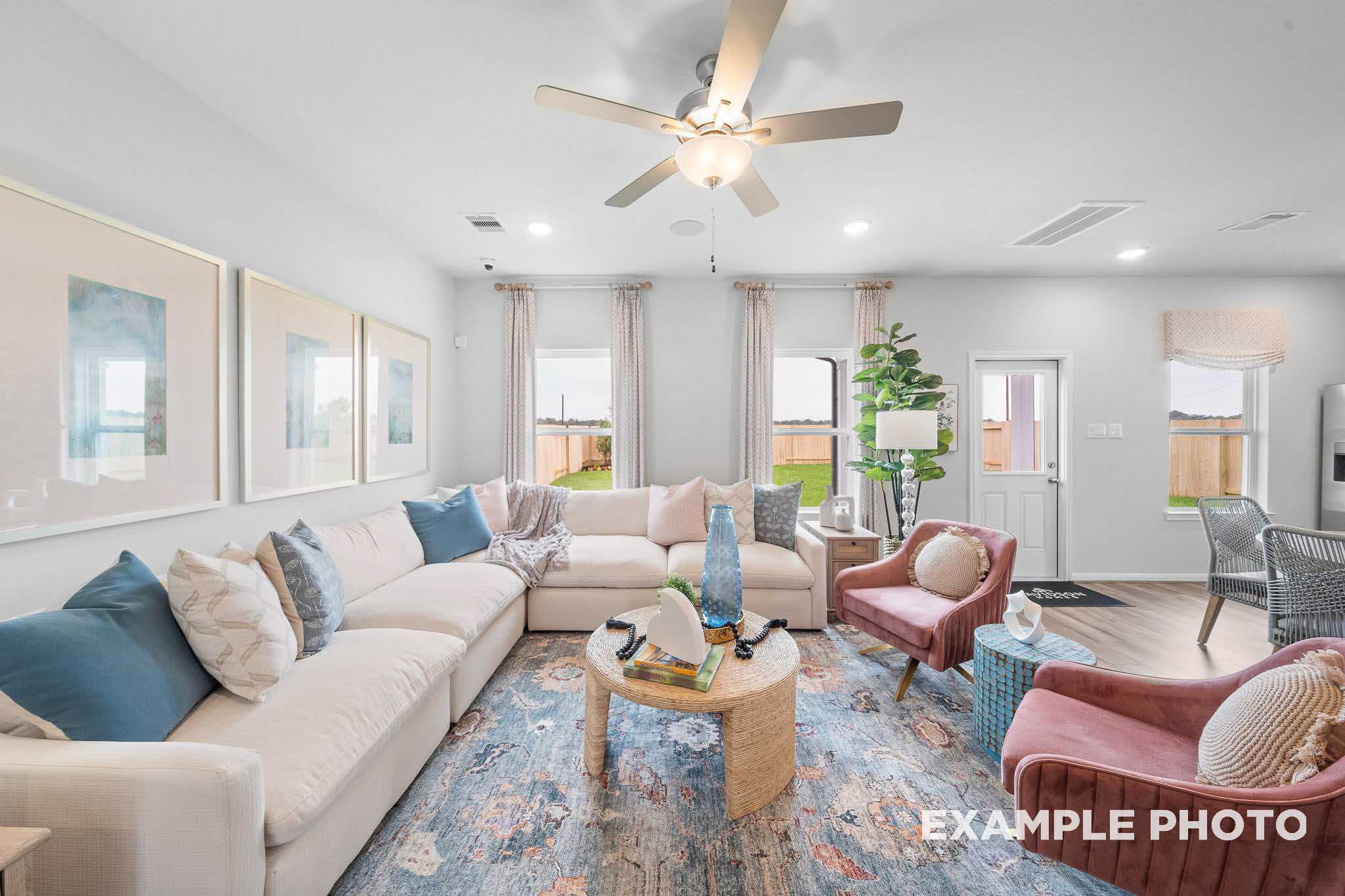 Spacious living room in The Trinity floor plan with L-shaped beige sofa, blue rug, ceiling fan, and modern abstract art