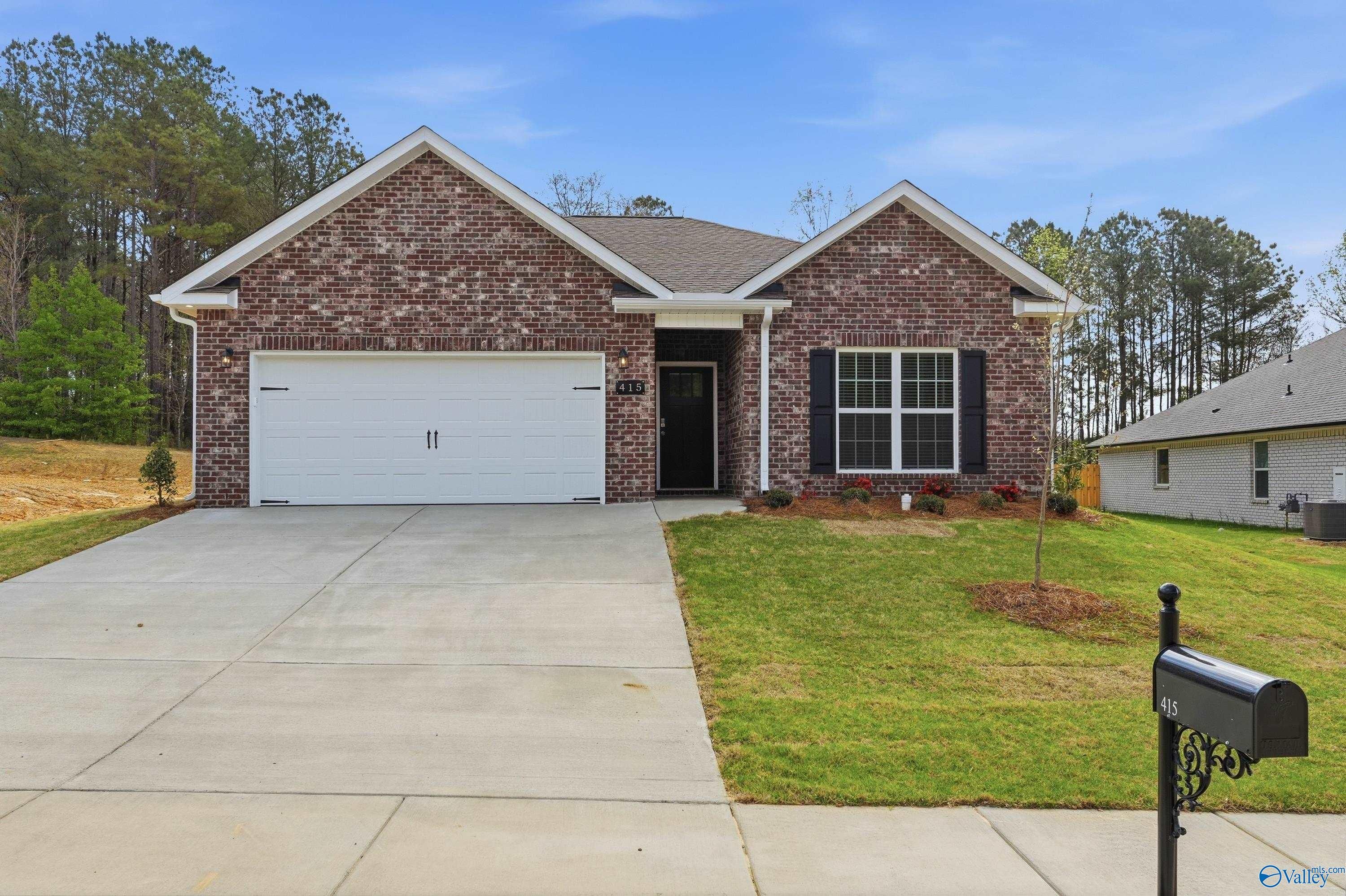 Red brick 1-story home with 2-car garage, white shutters, driveway, and lush front yard in The Highlands, Arab, Alabama - Davidson Homes Asheville C