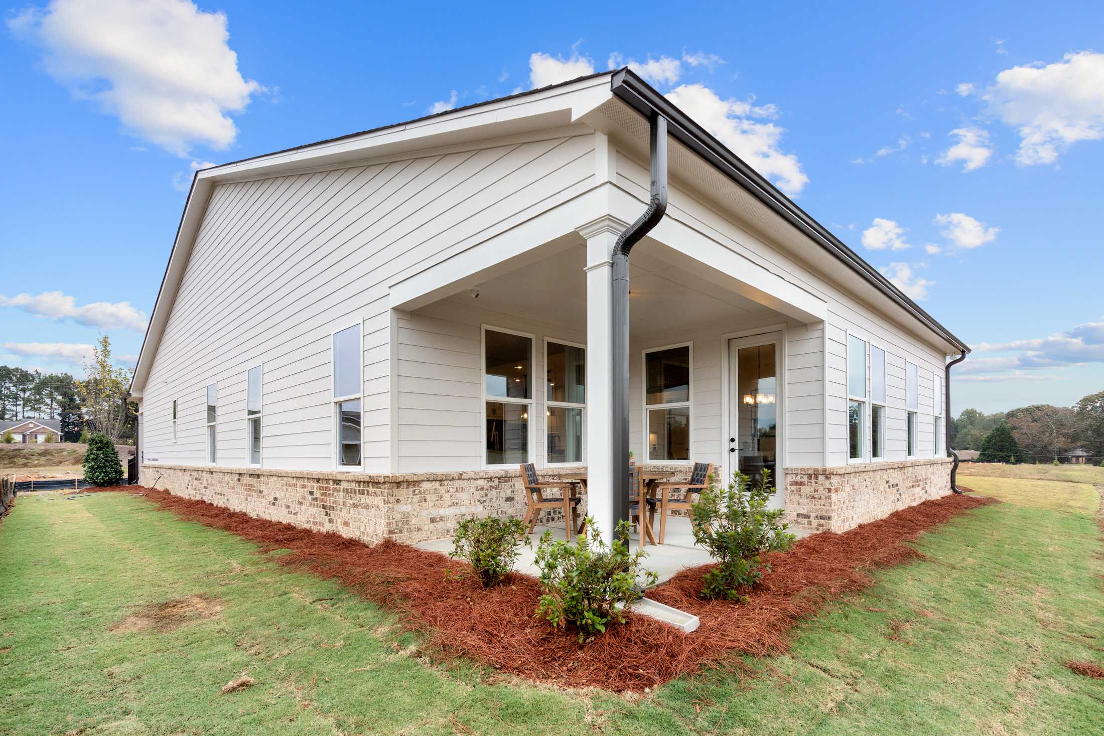 Contemporary home side exterior at Kelly Preserve in Loganville GA featuring covered porch with columns, large windows, patio furniture, and landscaped yard