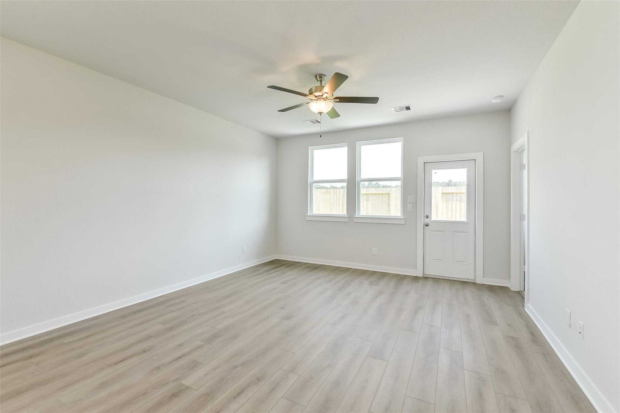 Spacious empty living room with ceiling fan, large windows, white walls, and light wood floors in Davidson Homes The Colorado F, Cleveland Texas