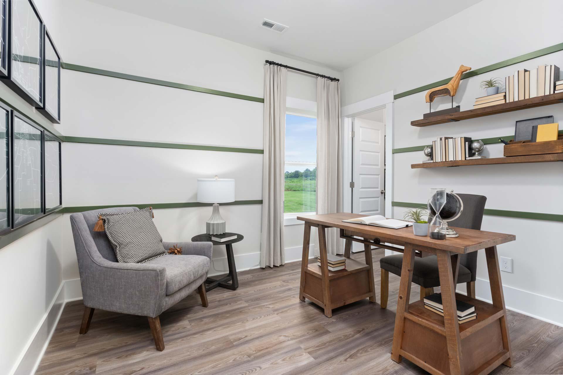 Cozy home office in The Meadows Athens AL with wooden desk, gray armchair, bookshelves, and window view of green fields