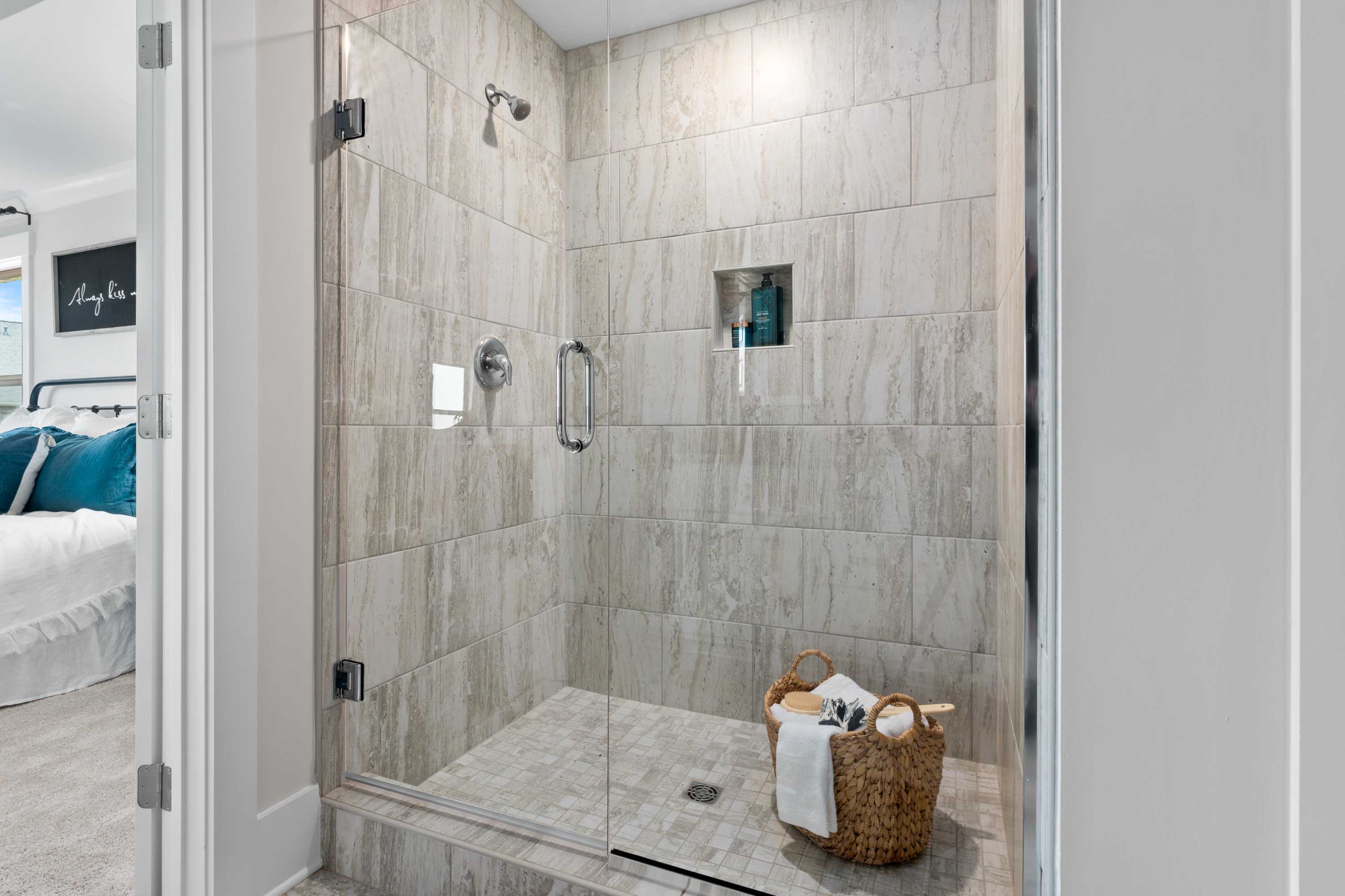 Modern master suite shower in The Chelsea B featuring frameless glass enclosure, tiled walls, and towel basket