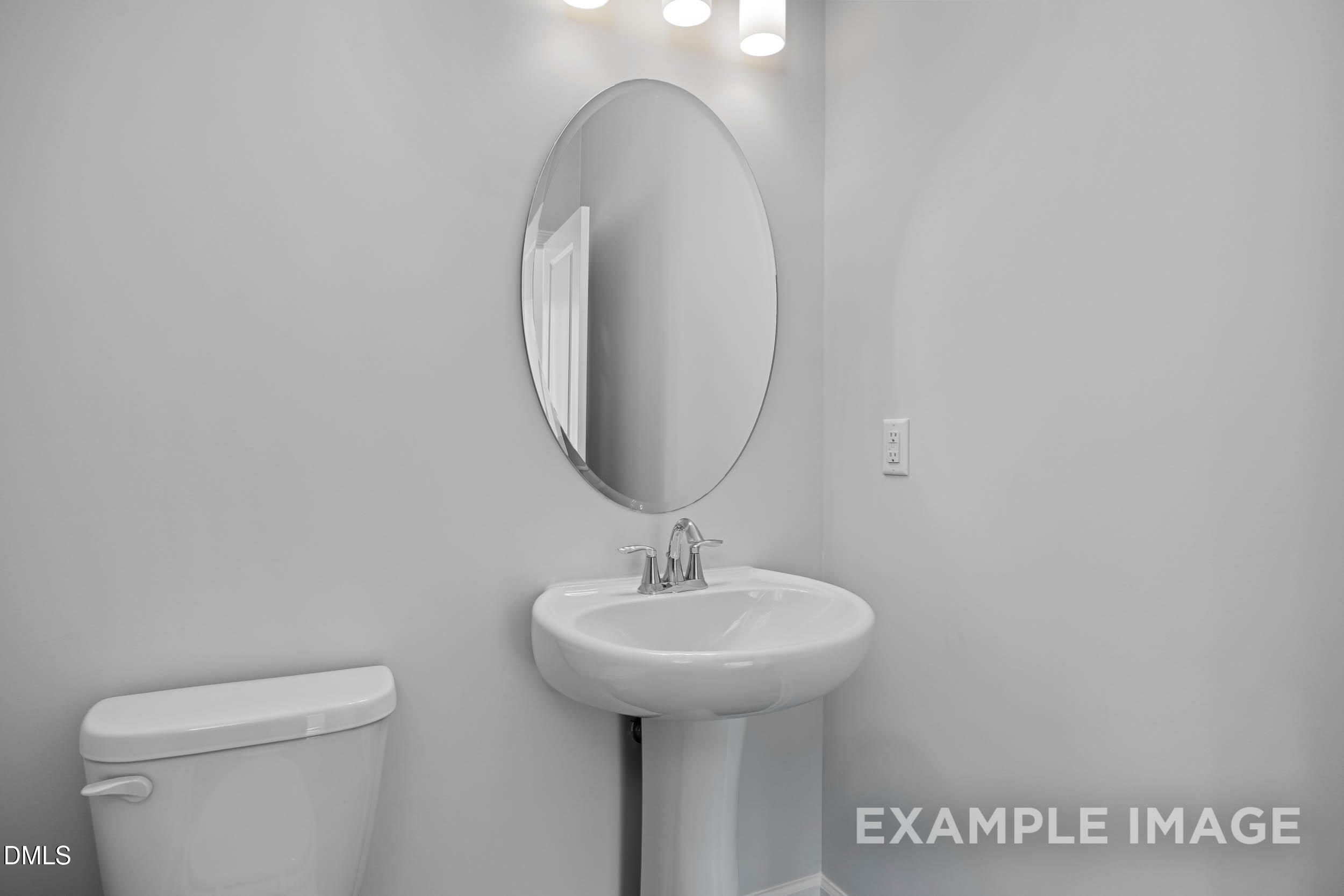 Elegant guest bathroom with white pedestal sink, round mirror, and toilet in Davidson Homes The Ash B, Lillington, NC