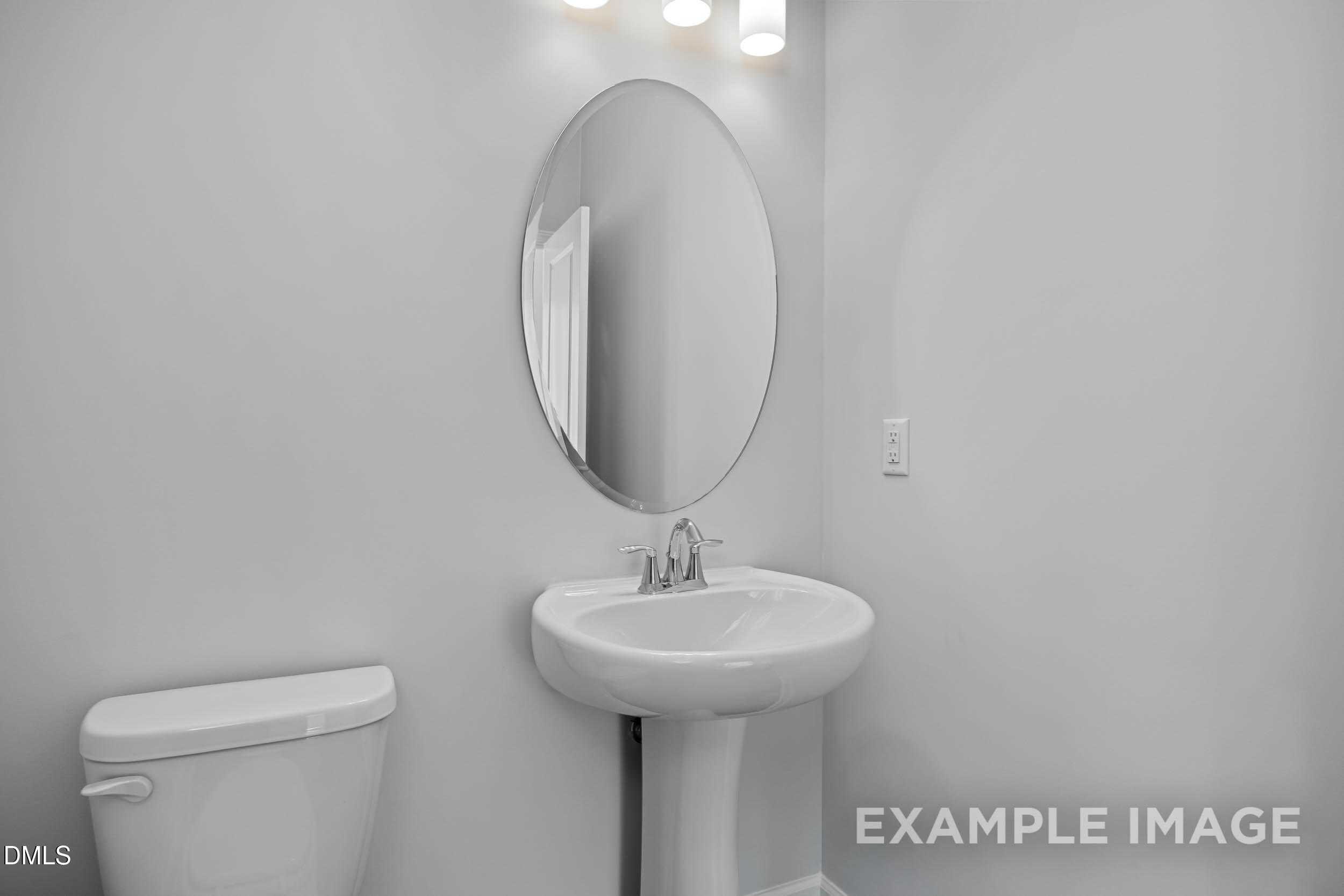 Elegant guest bathroom with white pedestal sink, round mirror, and toilet in Davidson Homes The Ash B, Lillington, NC