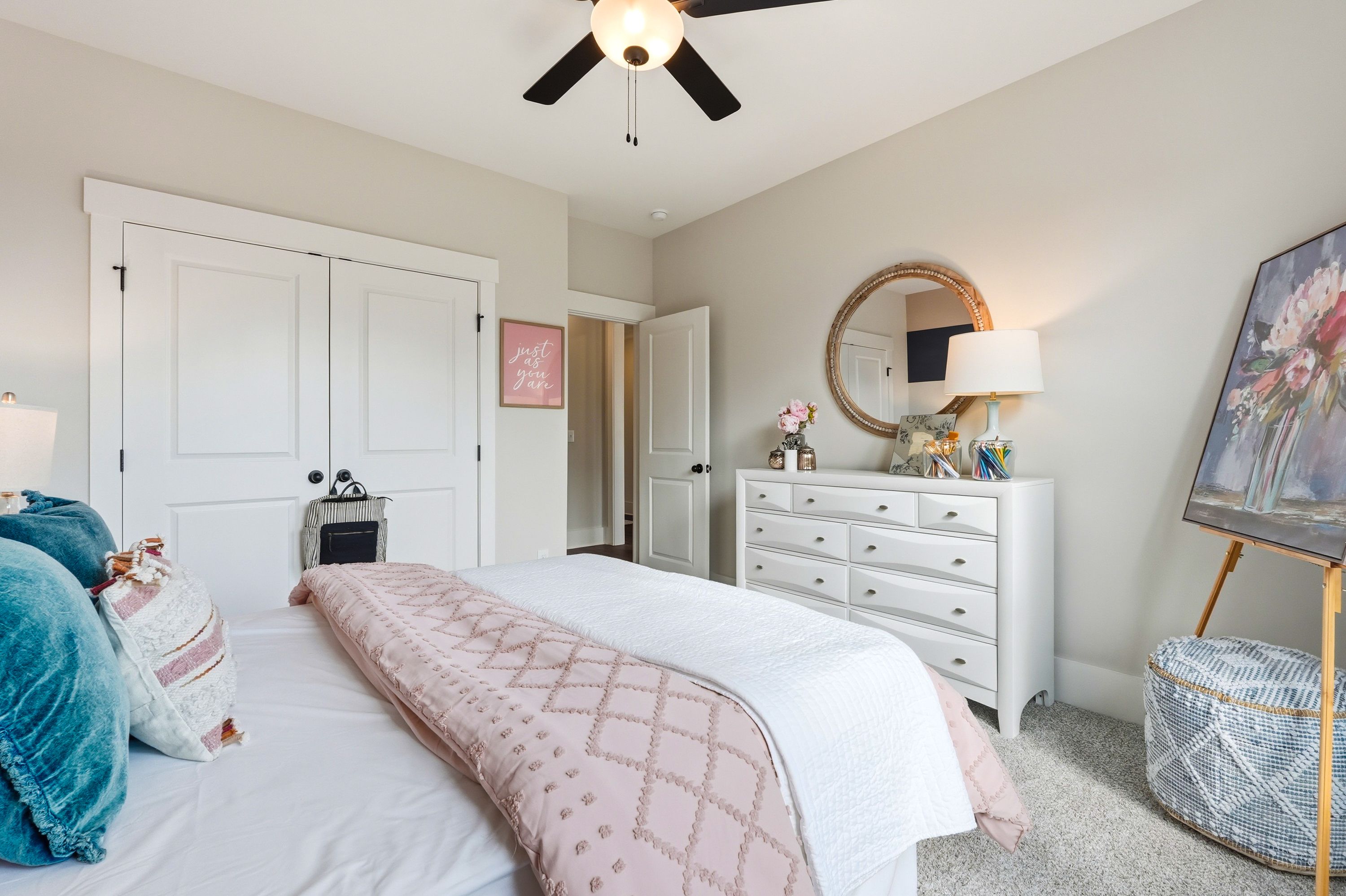 Cozy bedroom interior in Noble Ridge Cullman Alabama with white bed pink quilt dresser mirror and beige walls