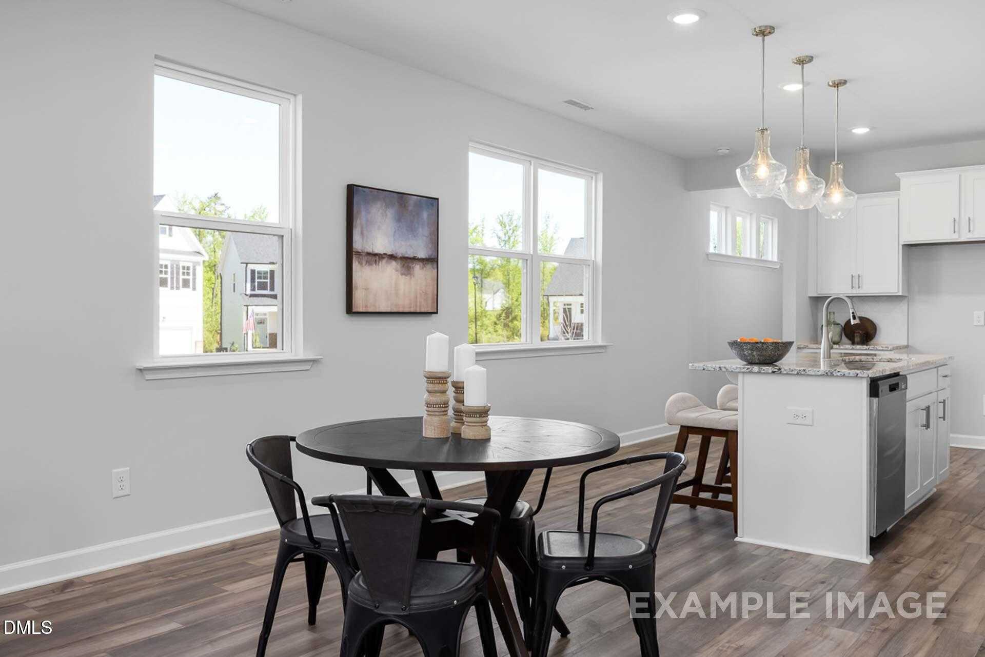 Open-concept dining area with round black table, pendant lights, and adjacent white kitchen in The Carter C home, Lillington, NC