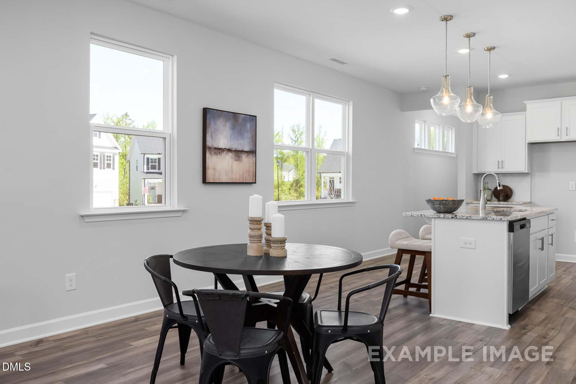 Open-concept dining area with round black table, chairs, and adjacent white kitchen island in Davidson Homes The Carter C, Lillington, NC
