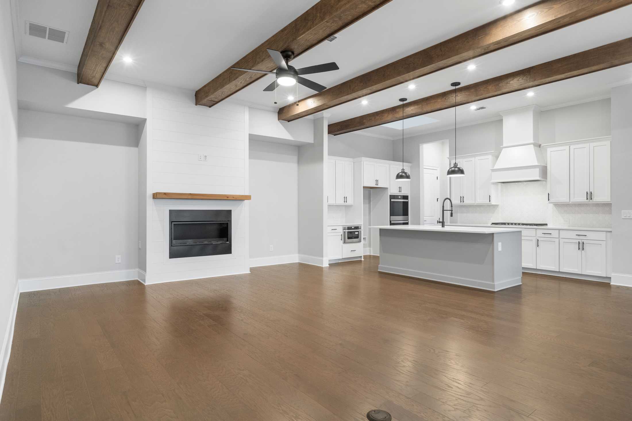 Spacious open-concept kitchen and family room in The Seaside Davidson Homes design featuring white cabinets, gray island, wood beam ceiling, and fireplace
