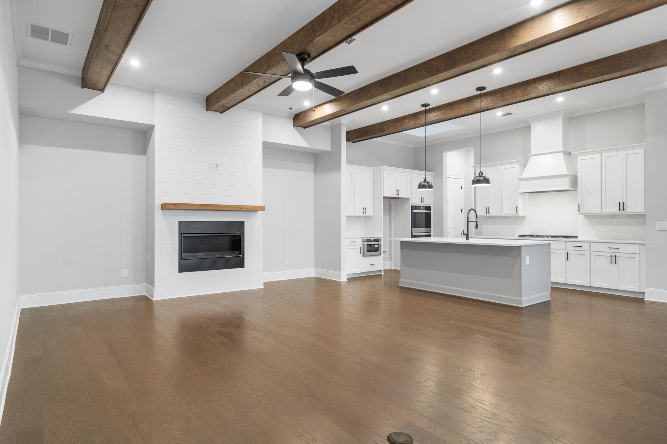 Spacious open-concept kitchen and family room in The Seaside Davidson Homes design featuring white cabinets, gray island, wood beam ceiling, and fireplace