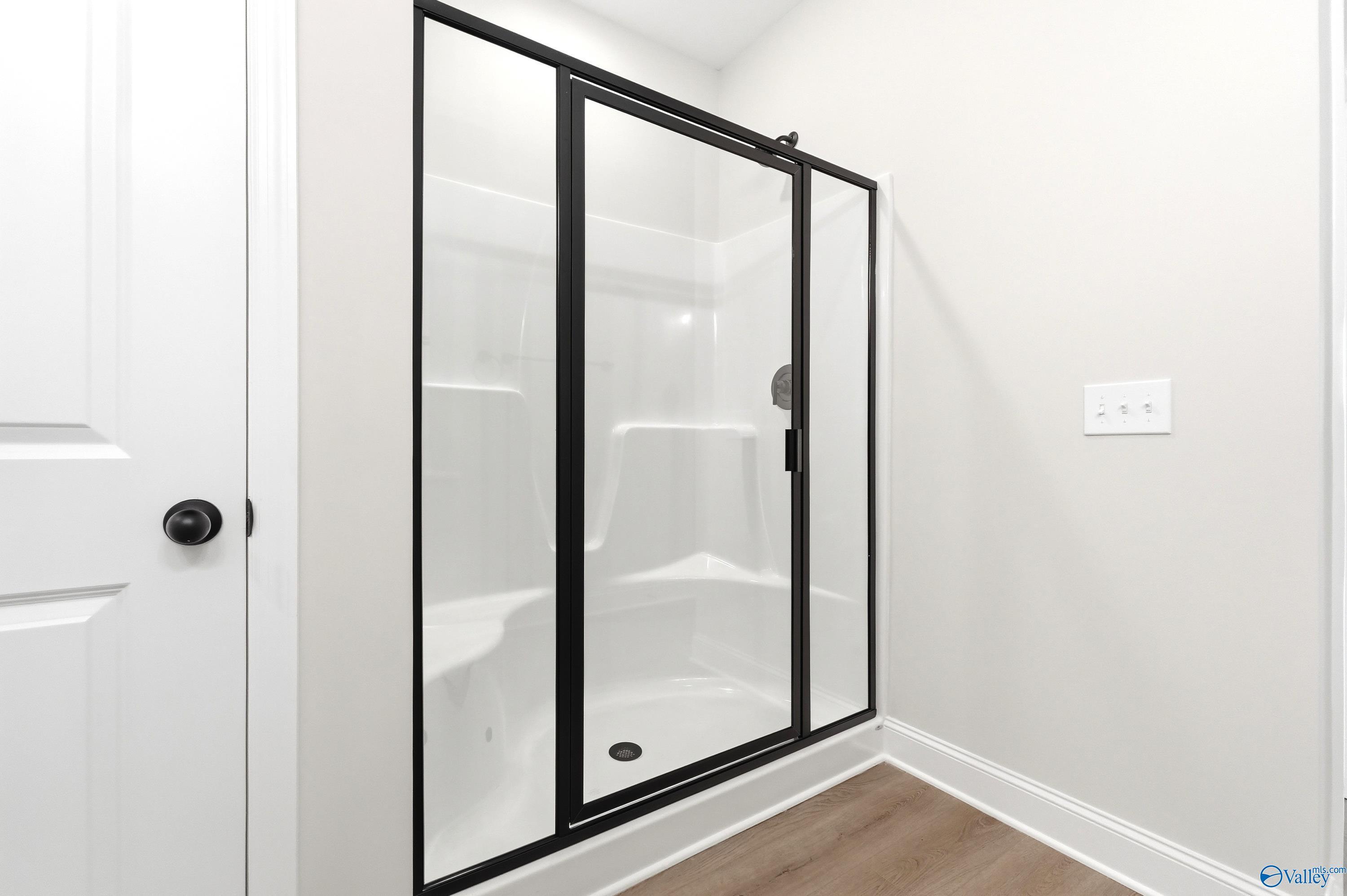 Modern walk-in shower with black frame and white surround in The Franklin floor plan at Ricketts Farm, Athens, Alabama.