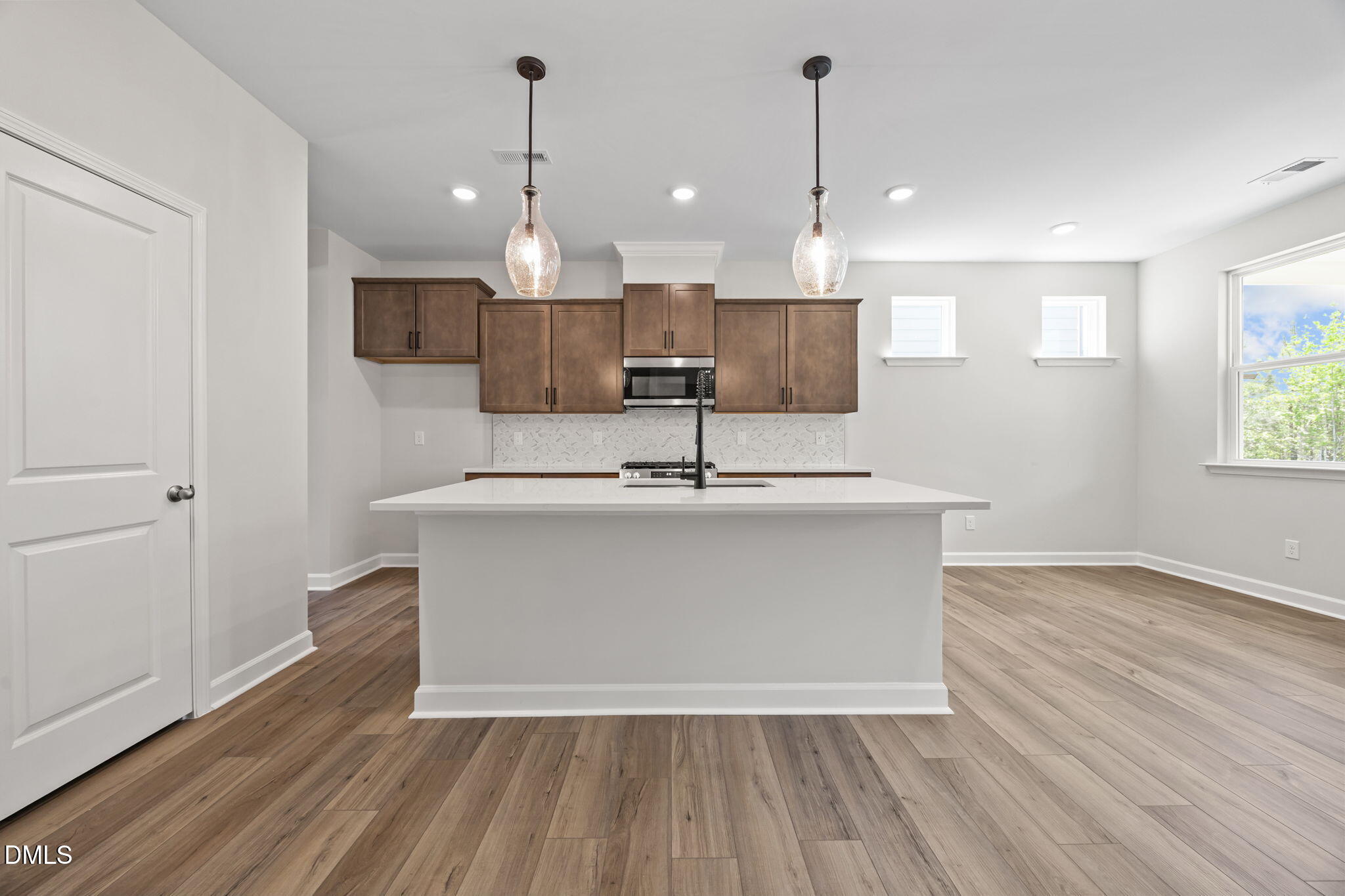 Bright open-concept kitchen with white quartz island, shaker cabinets, glass pendant lights in The Willow D, Wendell, NC