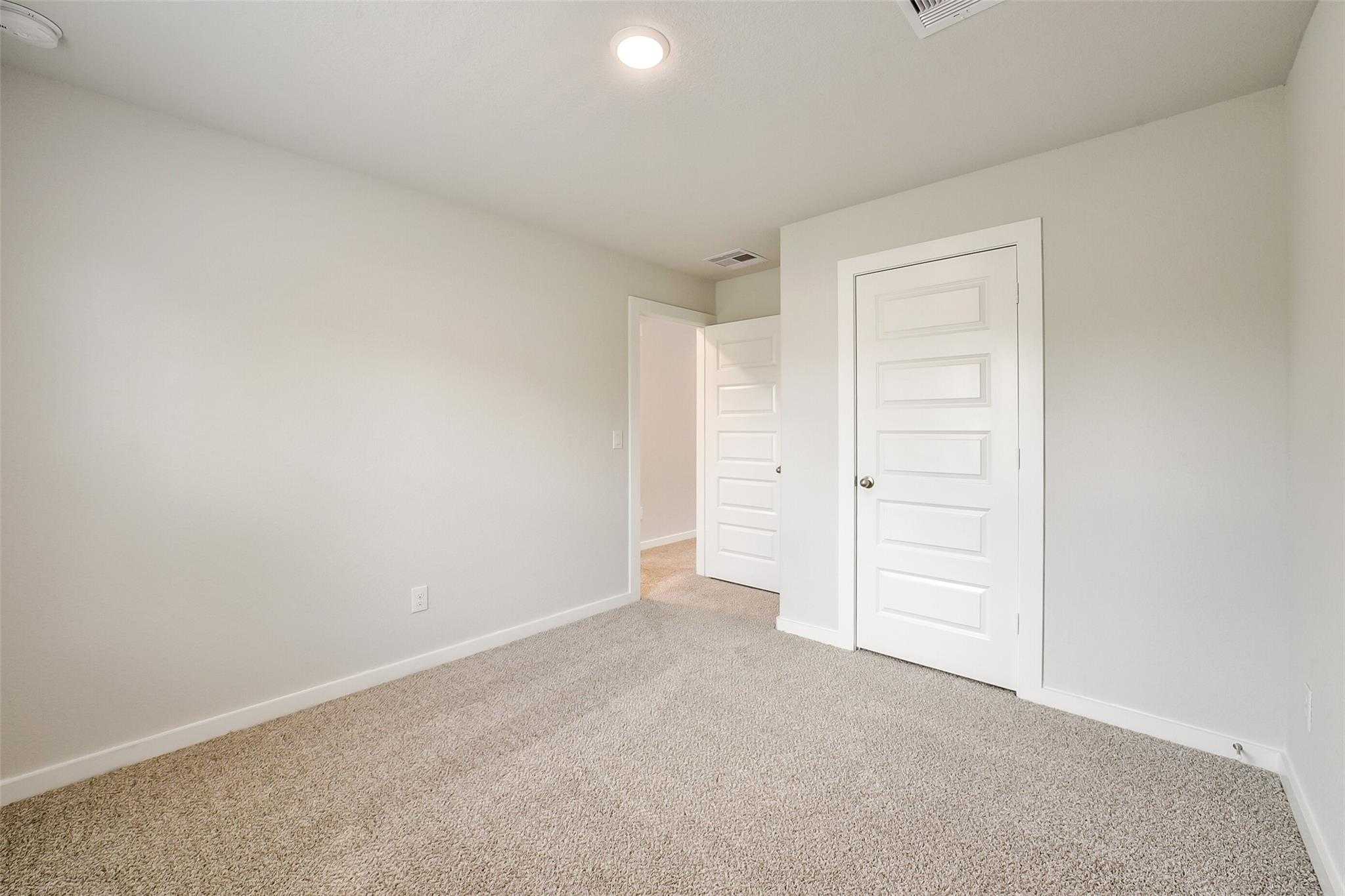 Spacious secondary bedroom featuring light gray walls, beige carpet, and white paneled doors in Davidson Homes The Trinity F, Magnolia, Texas