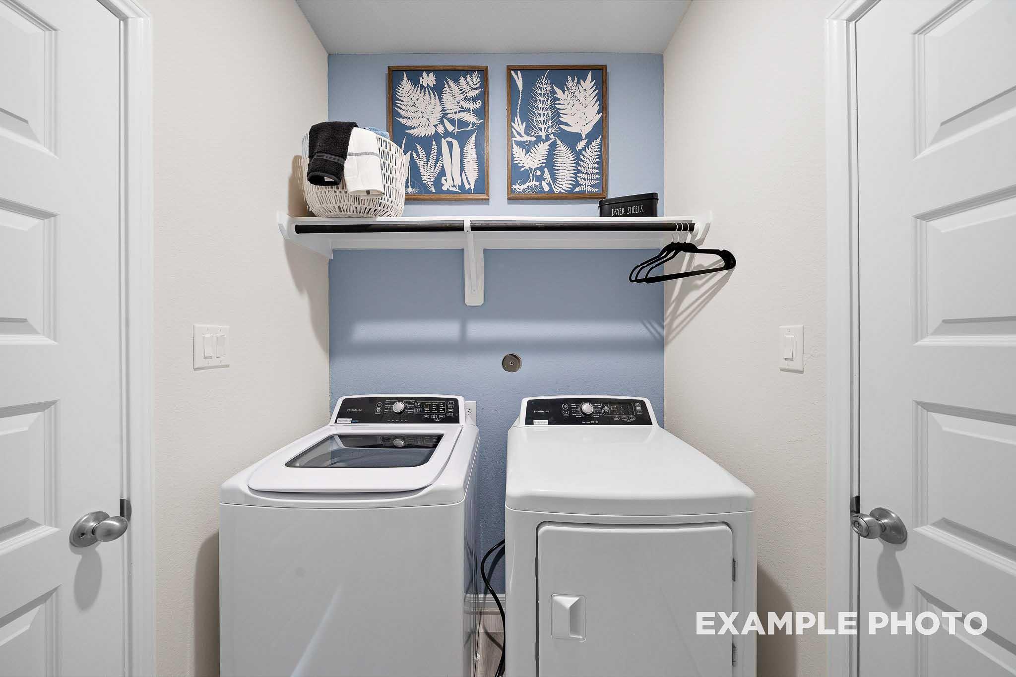 Spacious laundry room in The San Marcos Davidson Homes plan with white washer dryer, built-in shelves, and fern artwork