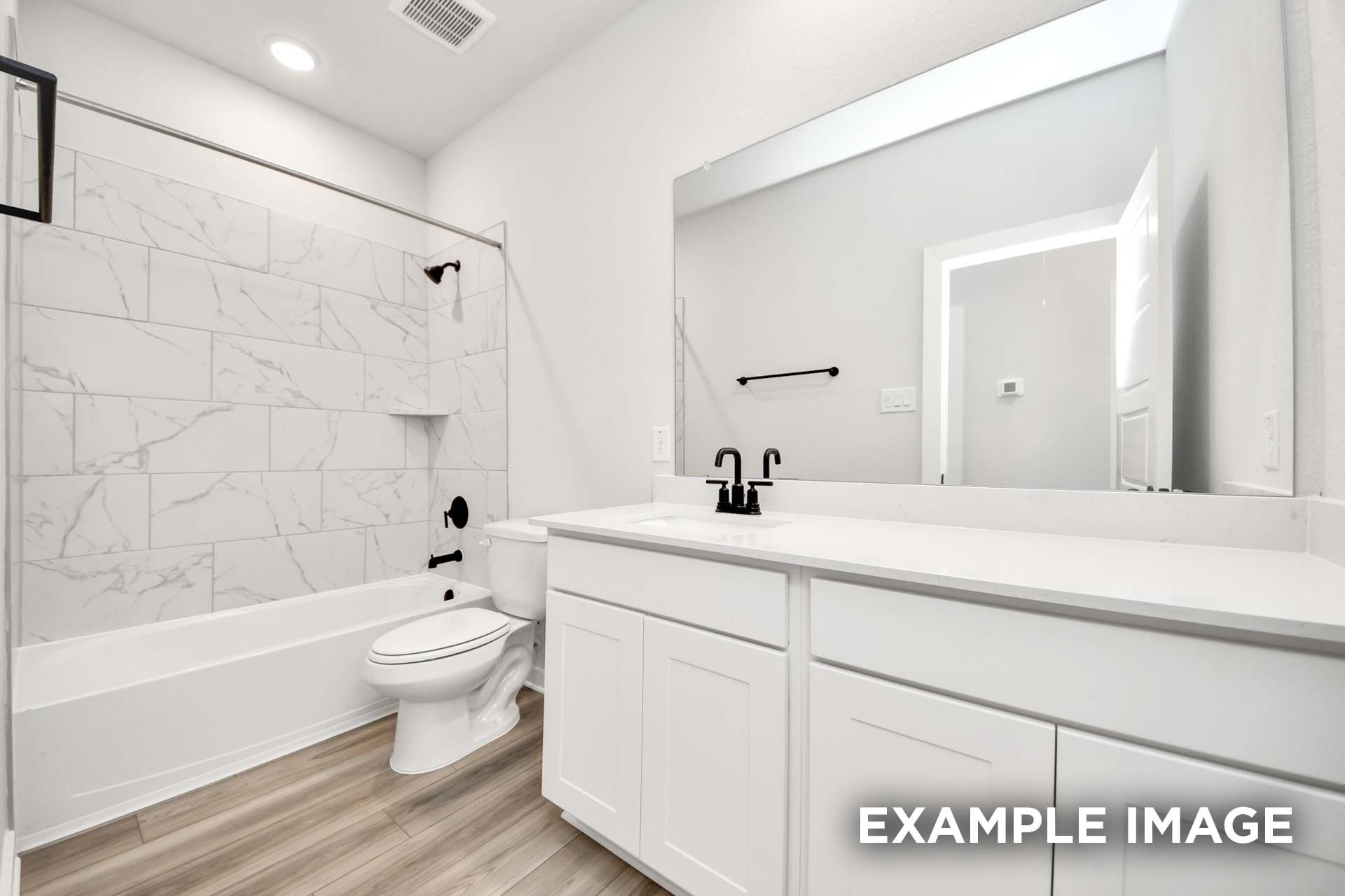 Modern bathroom in The Sorrento F featuring a white vanity, marble-style tile shower surround, and matte black fixtures.