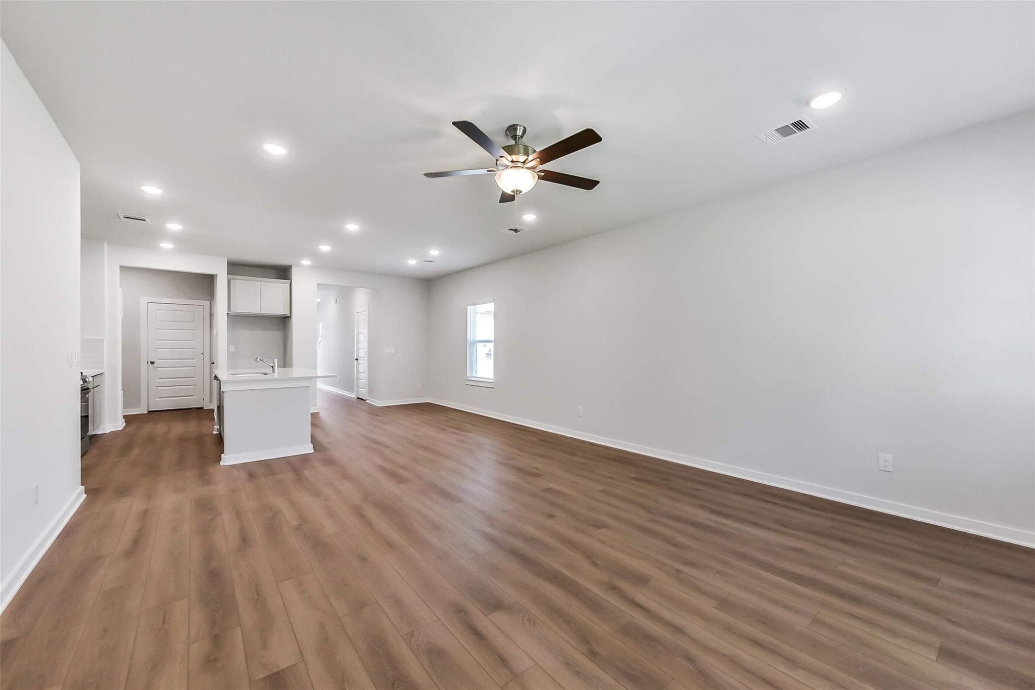 Open living space with white cabinets, kitchen island, hardwood floors, and ceiling fan in Davidson Homes The Brazos E, Magnolia, Texas